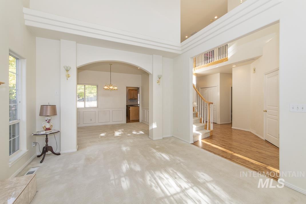 Carpeted empty room featuring a high ceiling, a chandelier, stairs, and arched walkways
