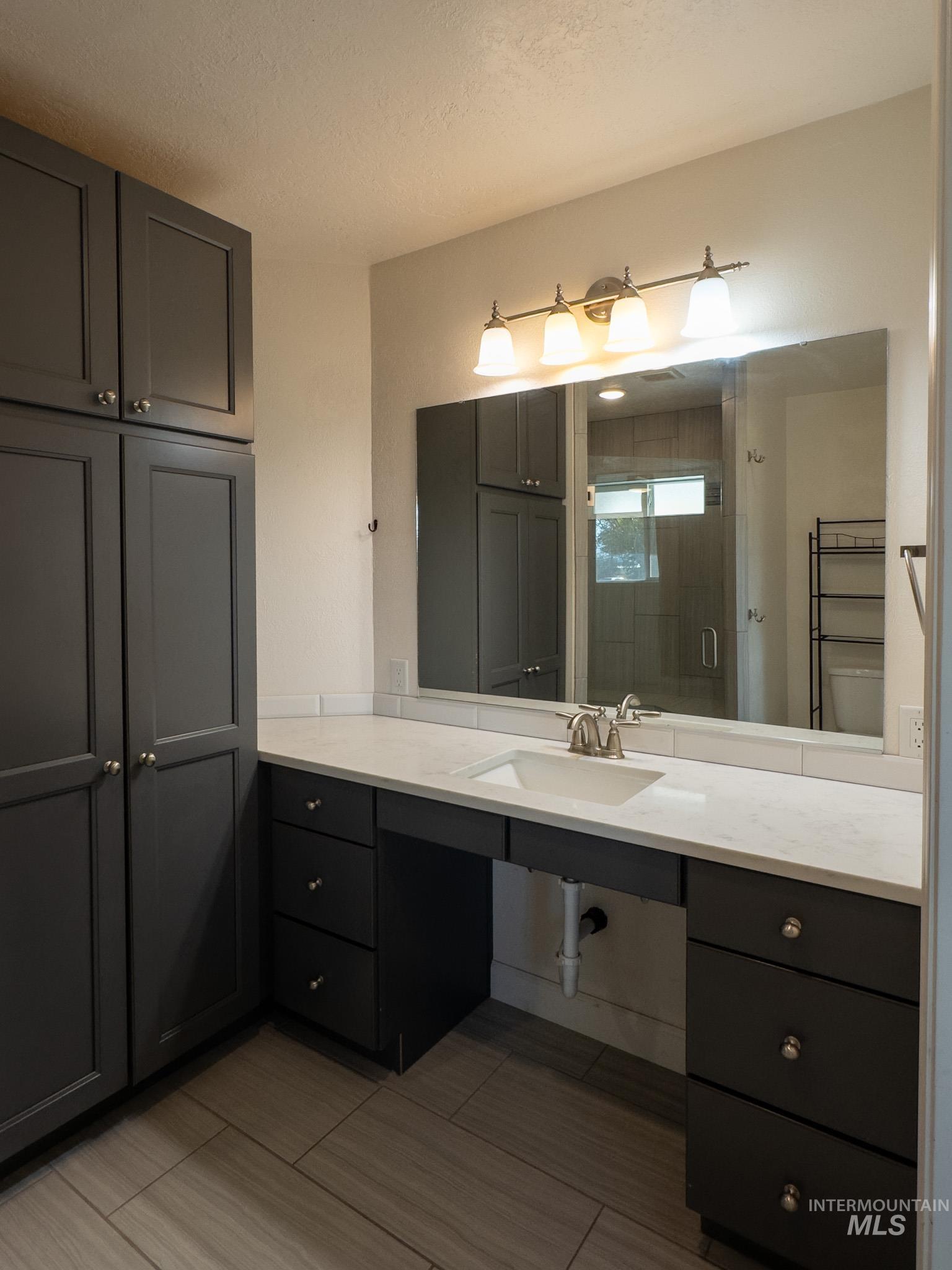 Master bath featuring roll-under vanity, curbless tile shower, and linen closet.