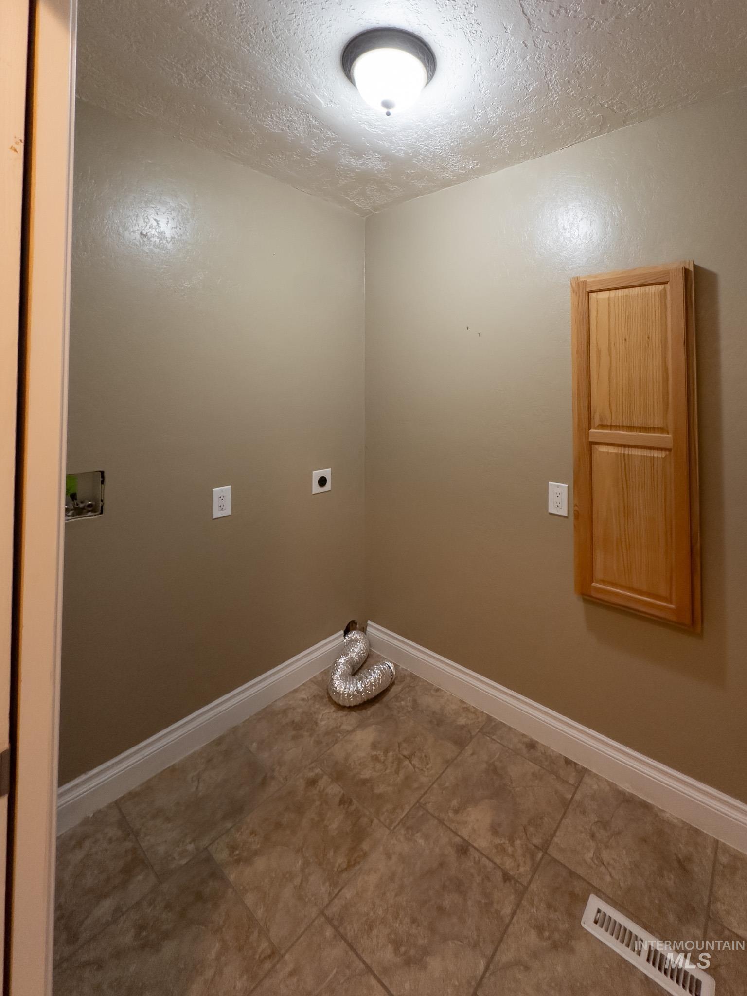 Washroom with a textured ceiling, electric dryer hookup, washer hookup, and light tile patterned floors