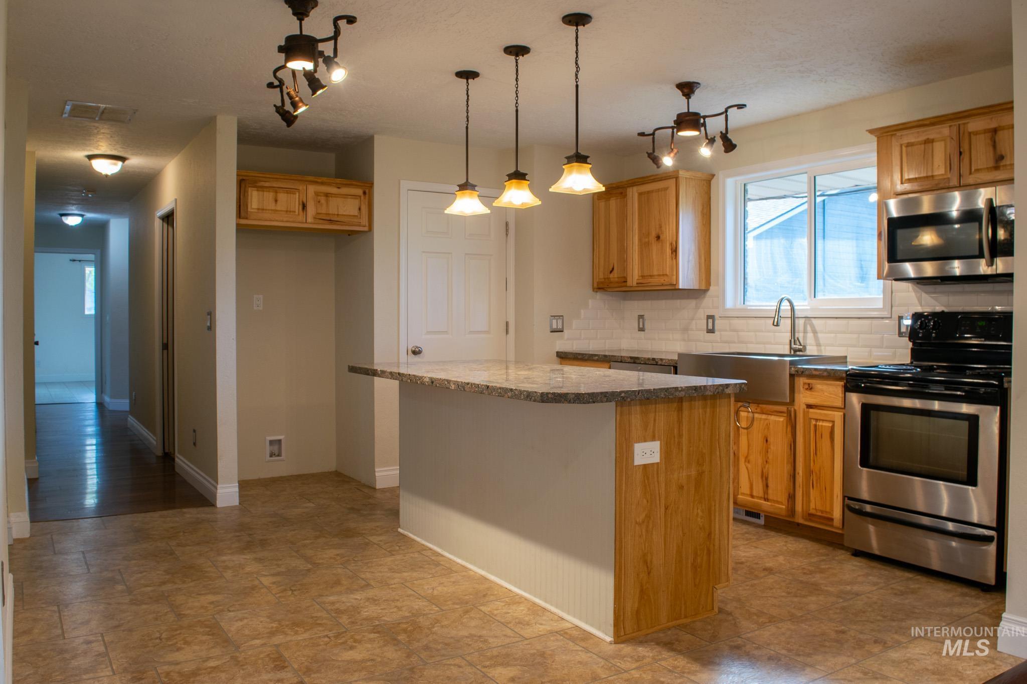 Kitchen with appliances with stainless steel finishes, backsplash, a center island, pendant lighting, and dark stone countertops