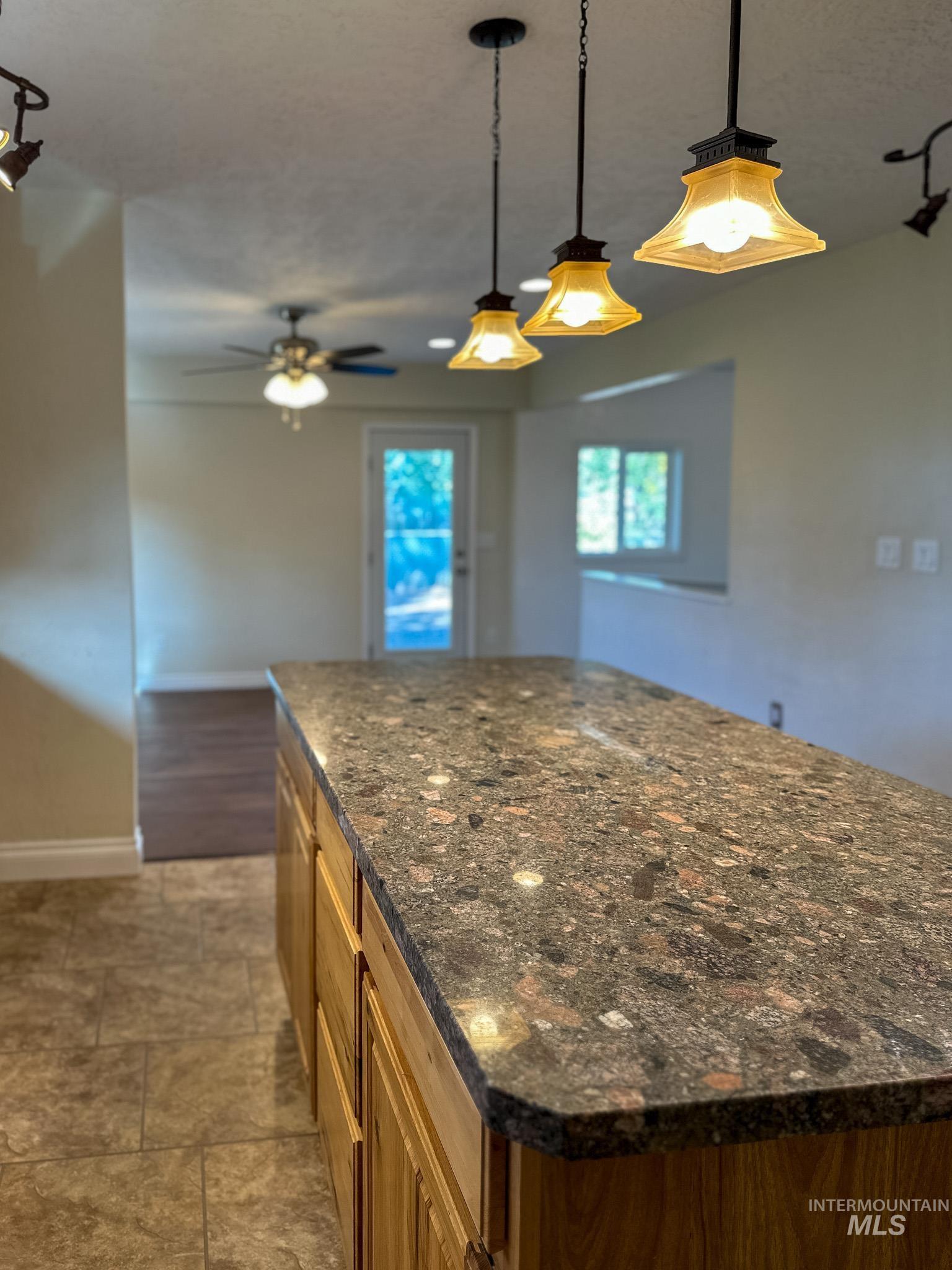 Kitchen featuring dark stone counters, decorative light fixtures, a kitchen island, and brown cabinetry