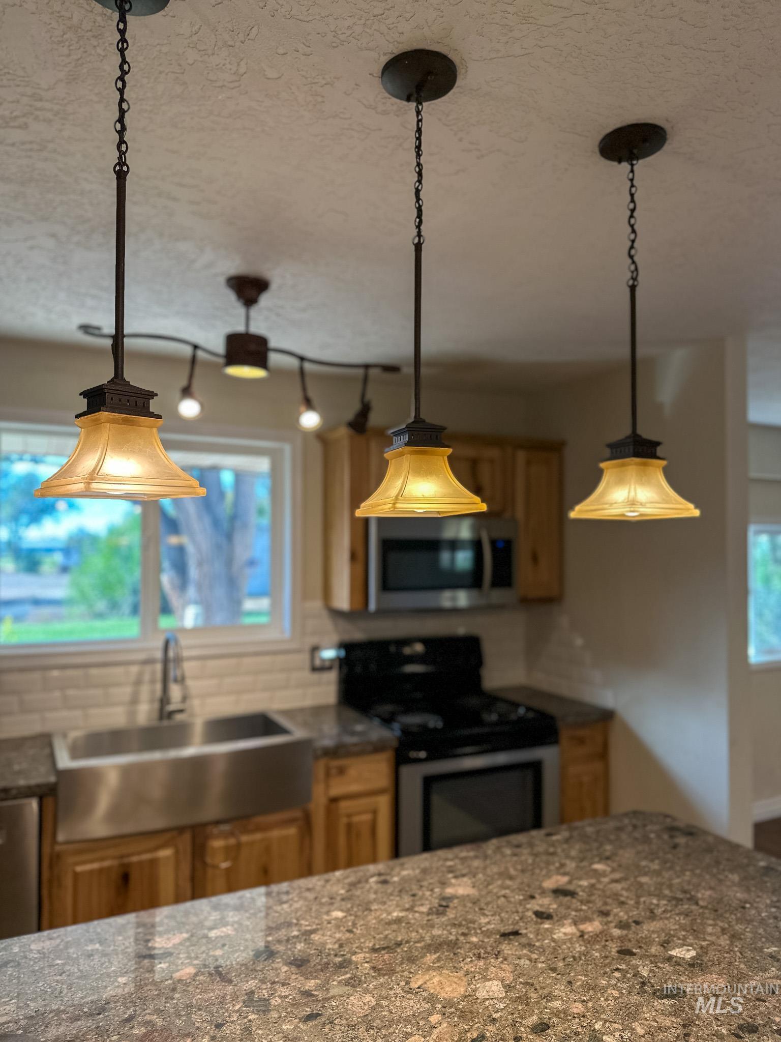 Kitchen with stainless steel appliances, dark stone counters, decorative backsplash, a textured ceiling, and decorative light fixtures