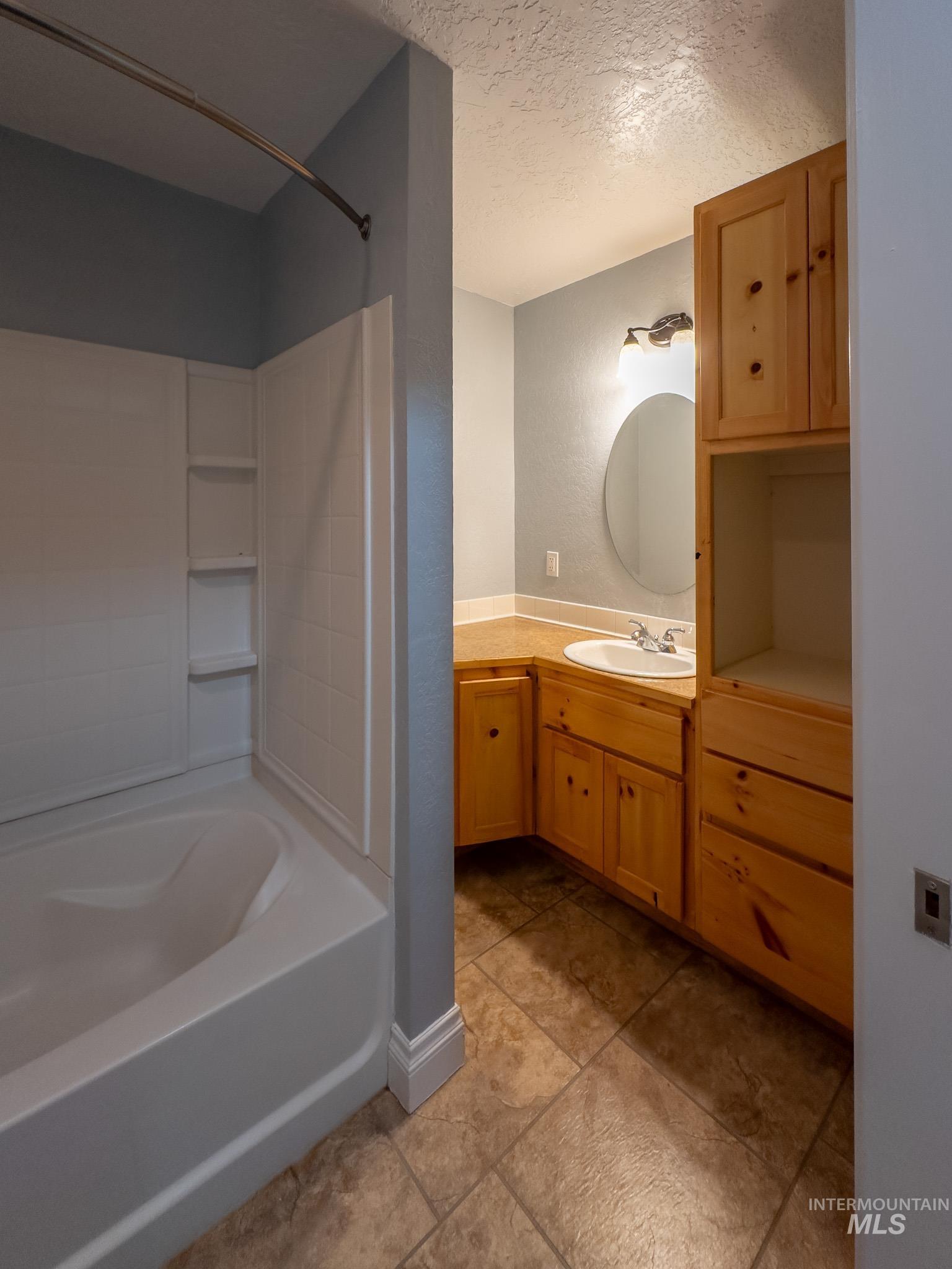 Full bath featuring a textured ceiling, vanity, a textured wall, washtub / shower combination, and light tile patterned floors