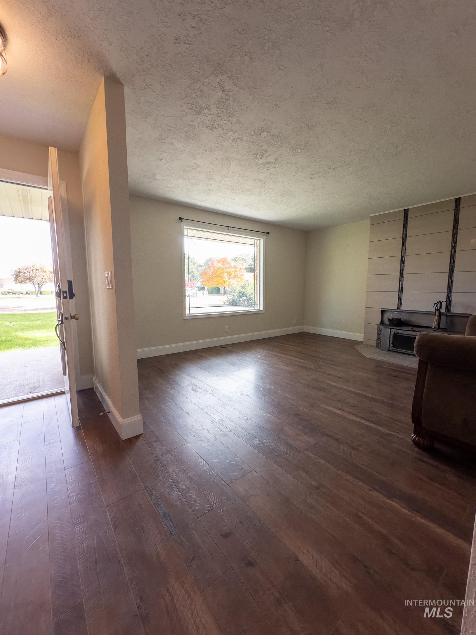 Unfurnished living room featuring a textured ceiling and dark wood-style flooring