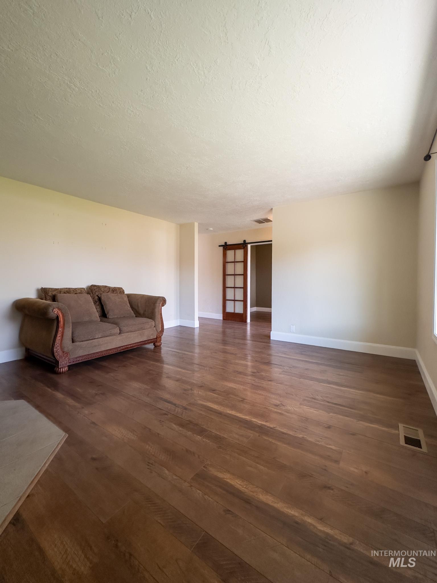 Living room featuring a barn door, a textured ceiling, and dark wood-style floors