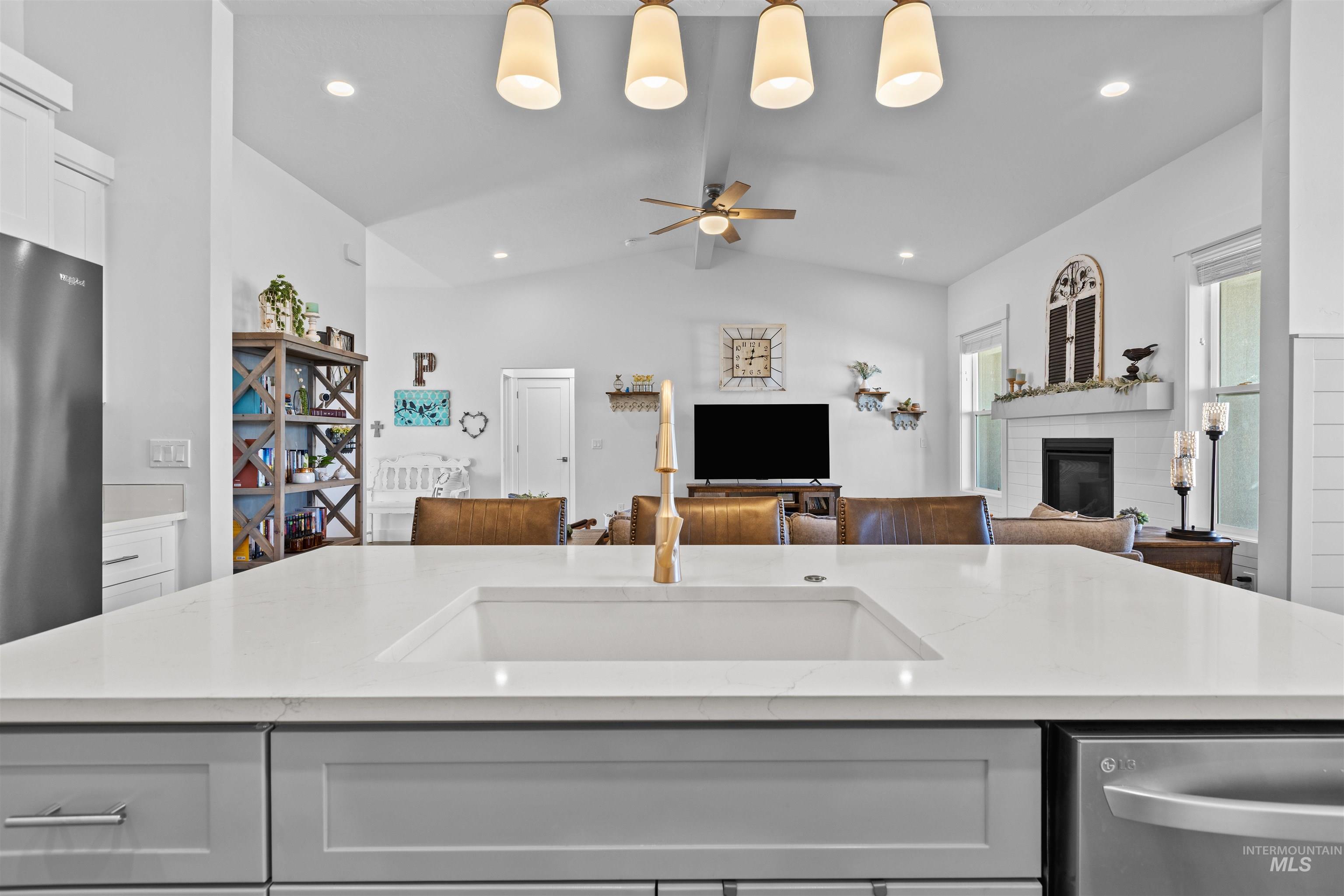 Kitchen featuring light stone counters, appliances with stainless steel finishes, vaulted ceiling, white cabinetry, and a ceiling fan
