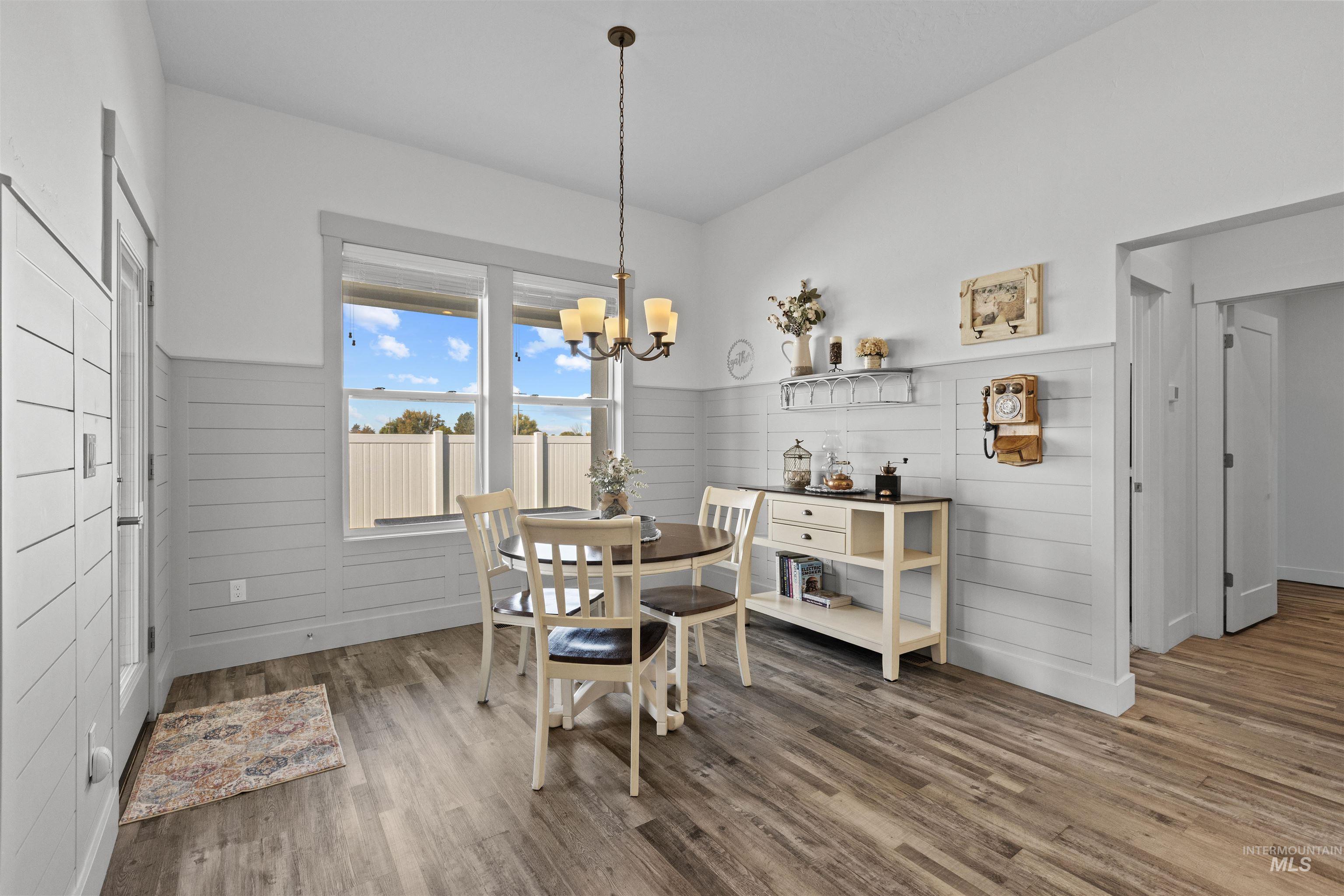 Dining room with wood finished floors, a chandelier, a wainscoted wall, and wood walls