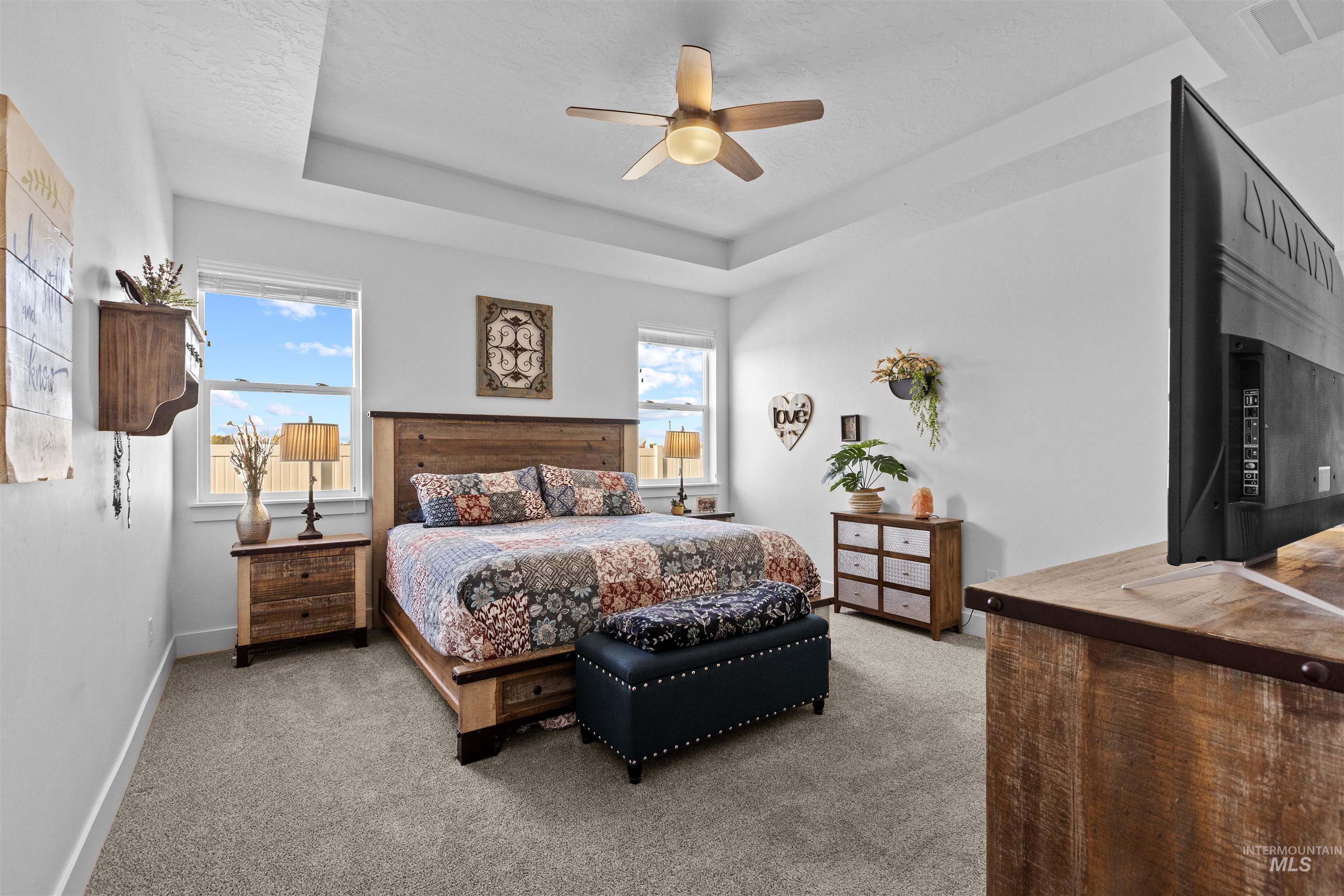 Bedroom with a raised ceiling, light carpet, and ceiling fan