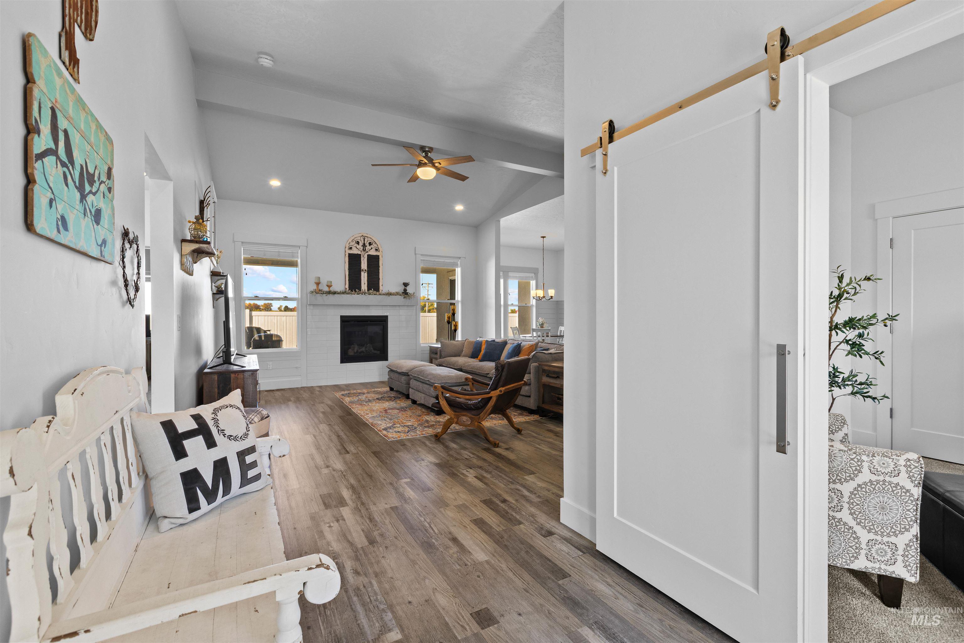 Living area with a barn door, ceiling fan, dark wood finished floors, vaulted ceiling, and a glass covered fireplace