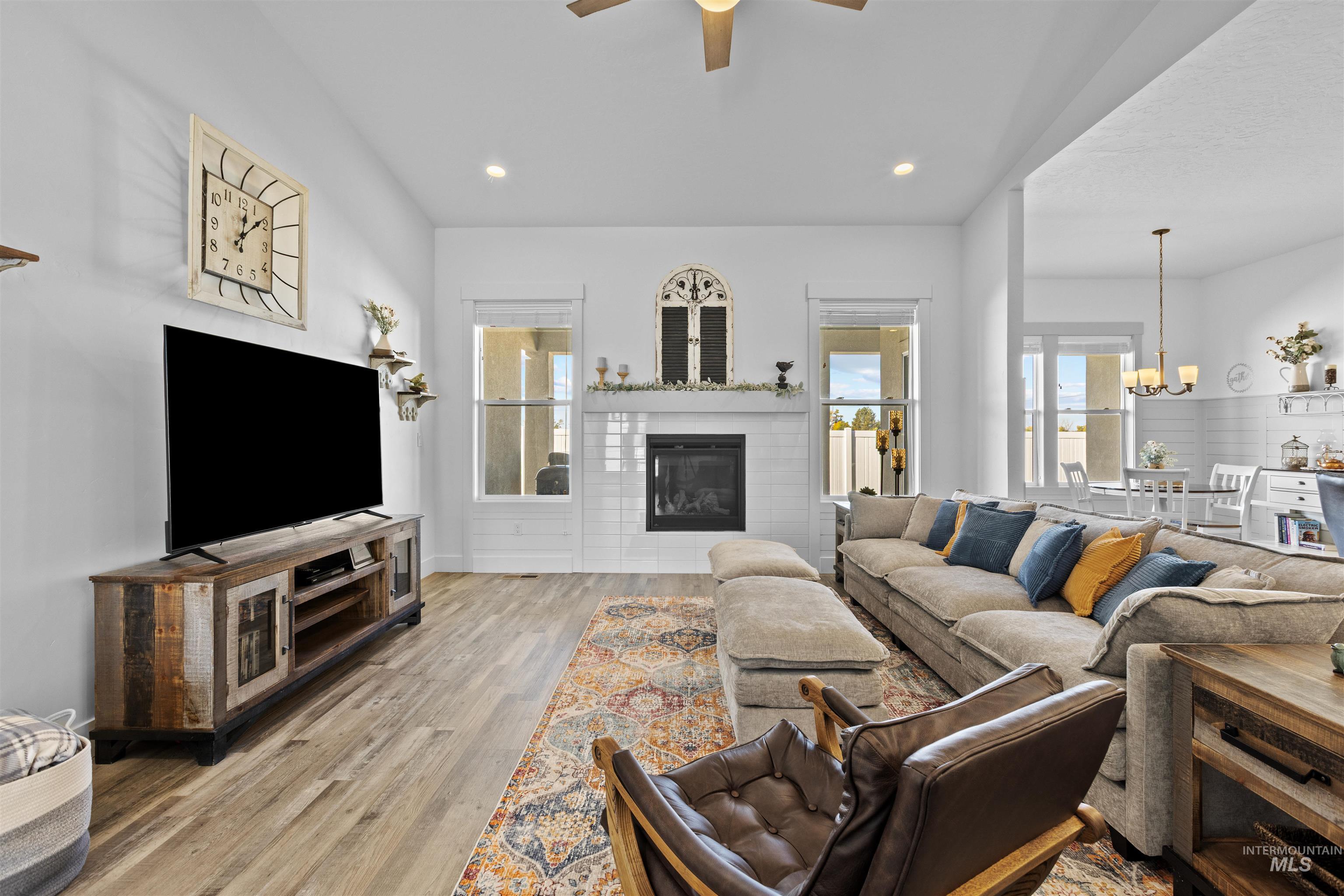 Living room with a glass covered fireplace, wood finished floors, a ceiling fan, a chandelier, and recessed lighting