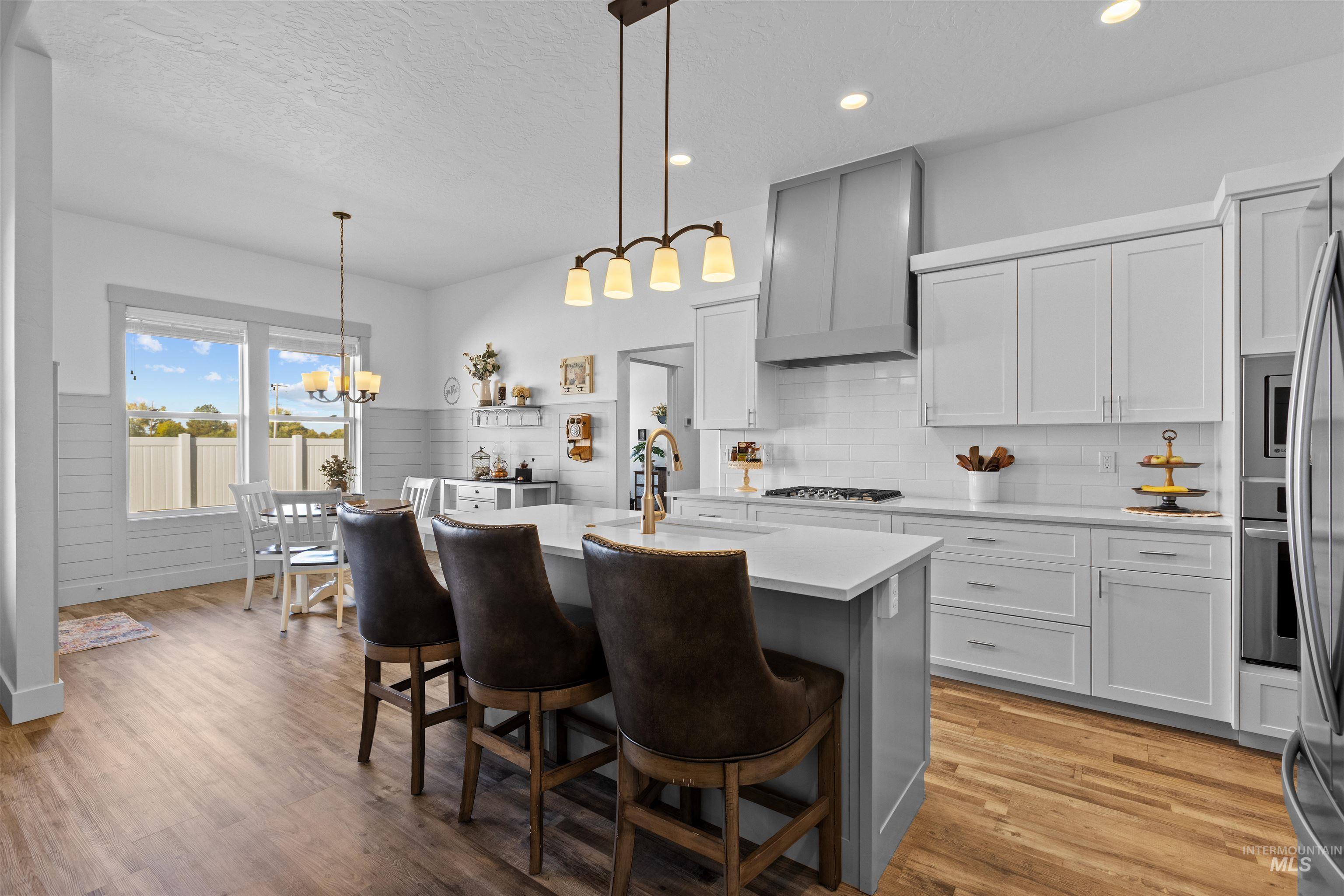 Kitchen featuring a center island with sink, tasteful backsplash, white cabinetry, pendant lighting, and light wood-type flooring