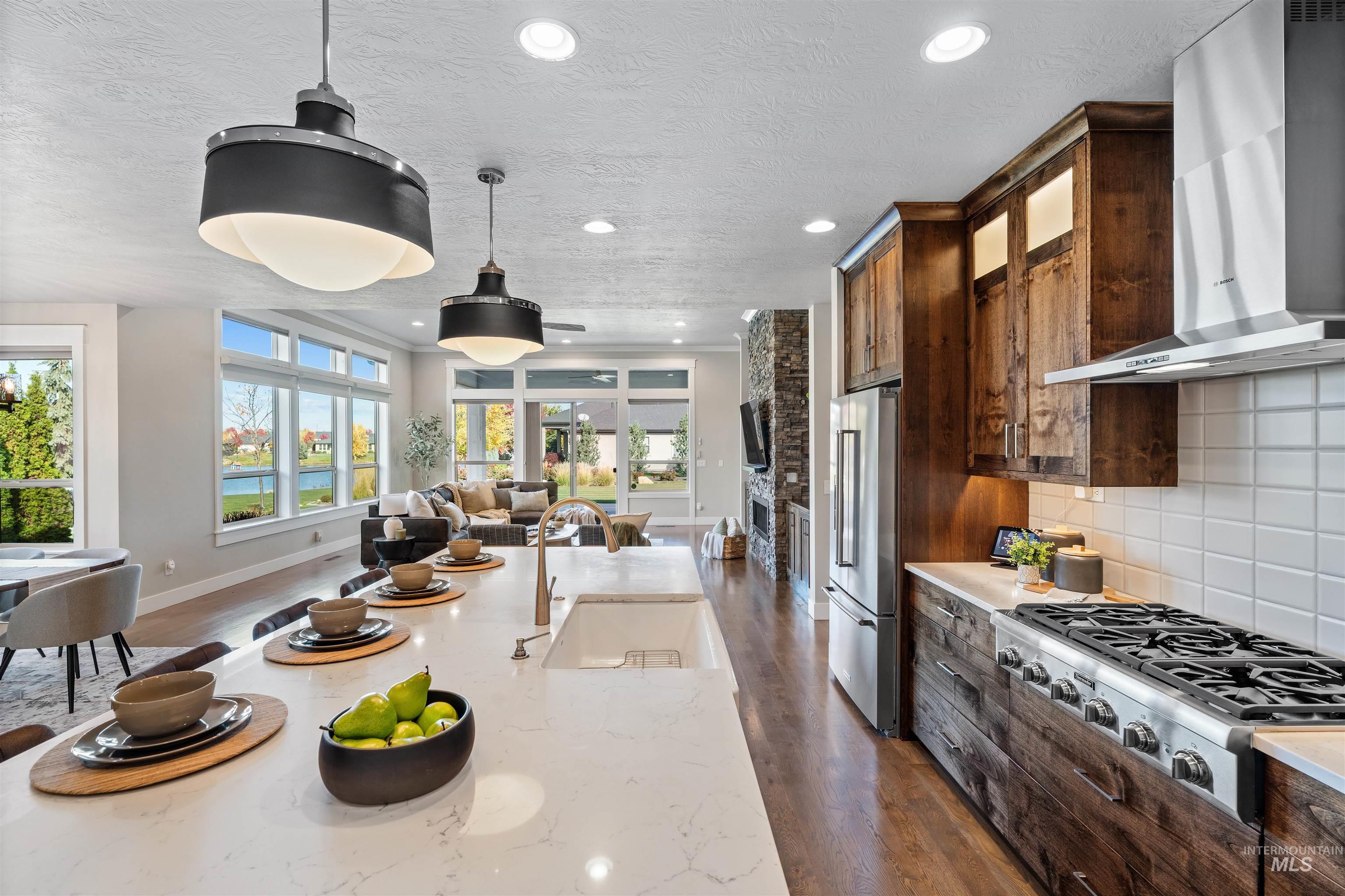 Kitchen featuring dark wood-type flooring, wall chimney exhaust hood, open floor plan, appliances with stainless steel finishes, and tasteful backsplash