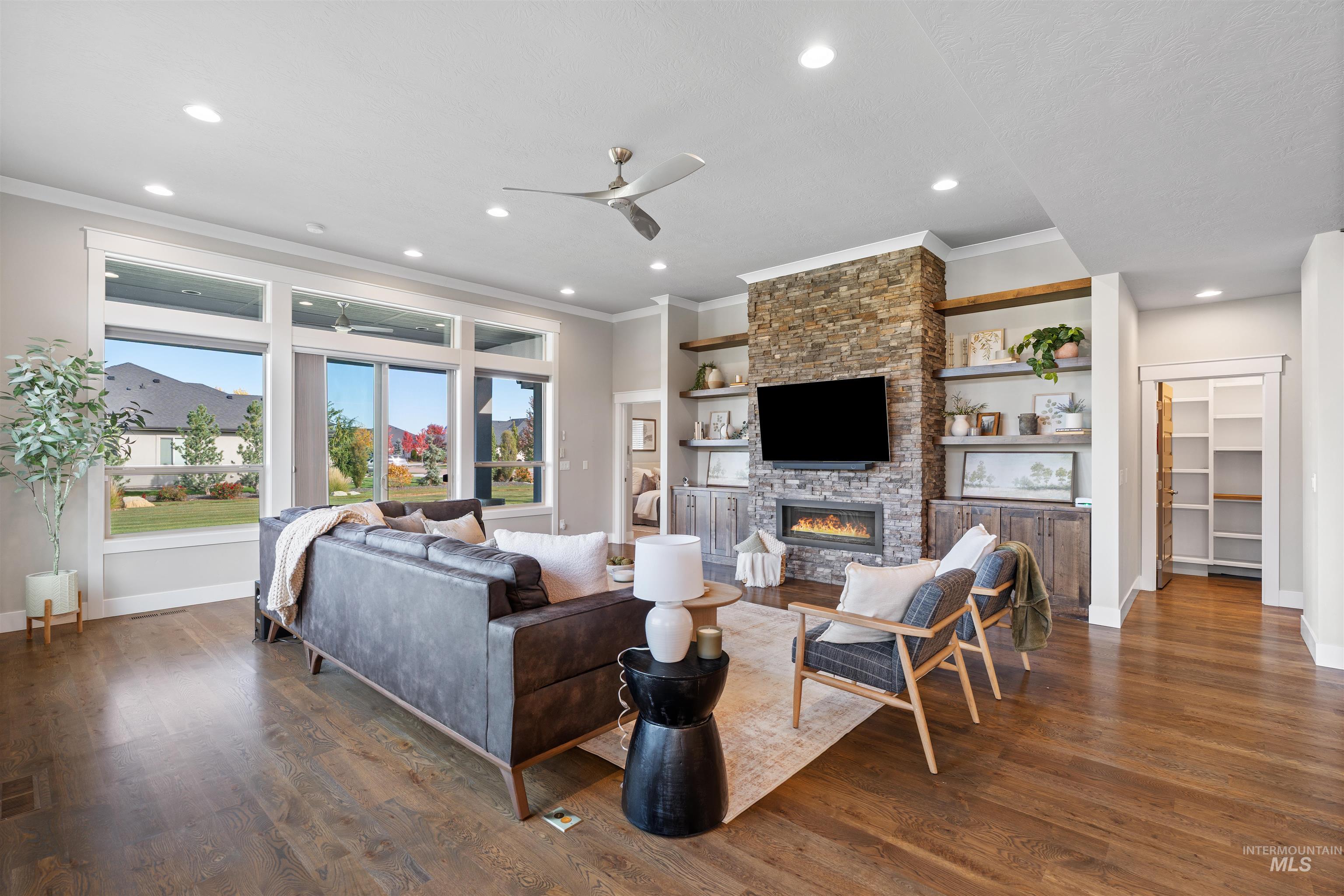 Living room featuring ceiling fan, a stone fireplace, dark wood finished floors, recessed lighting, and crown molding