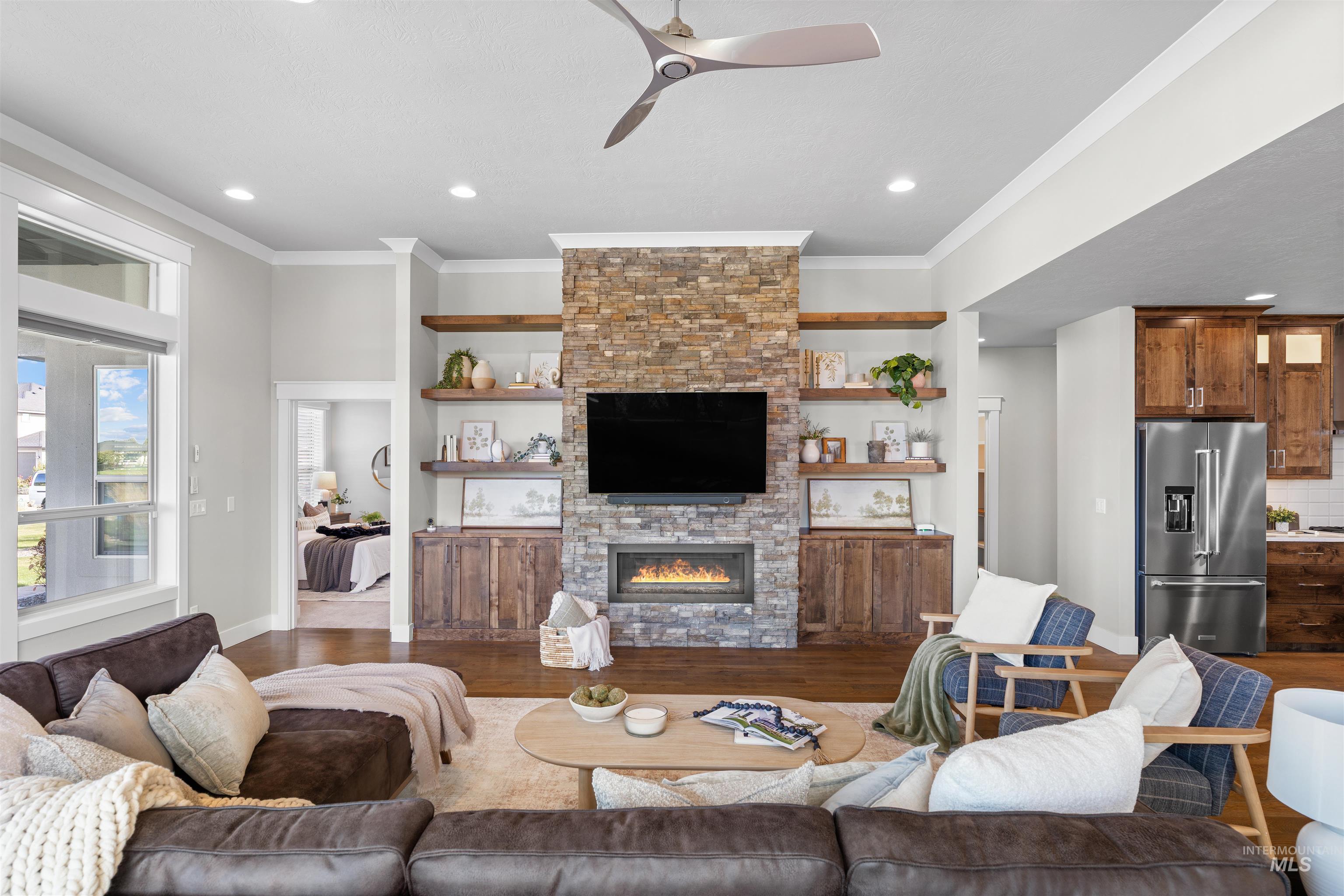 Living area featuring ceiling fan, wood finished floors, a stone fireplace, ornamental molding, and recessed lighting