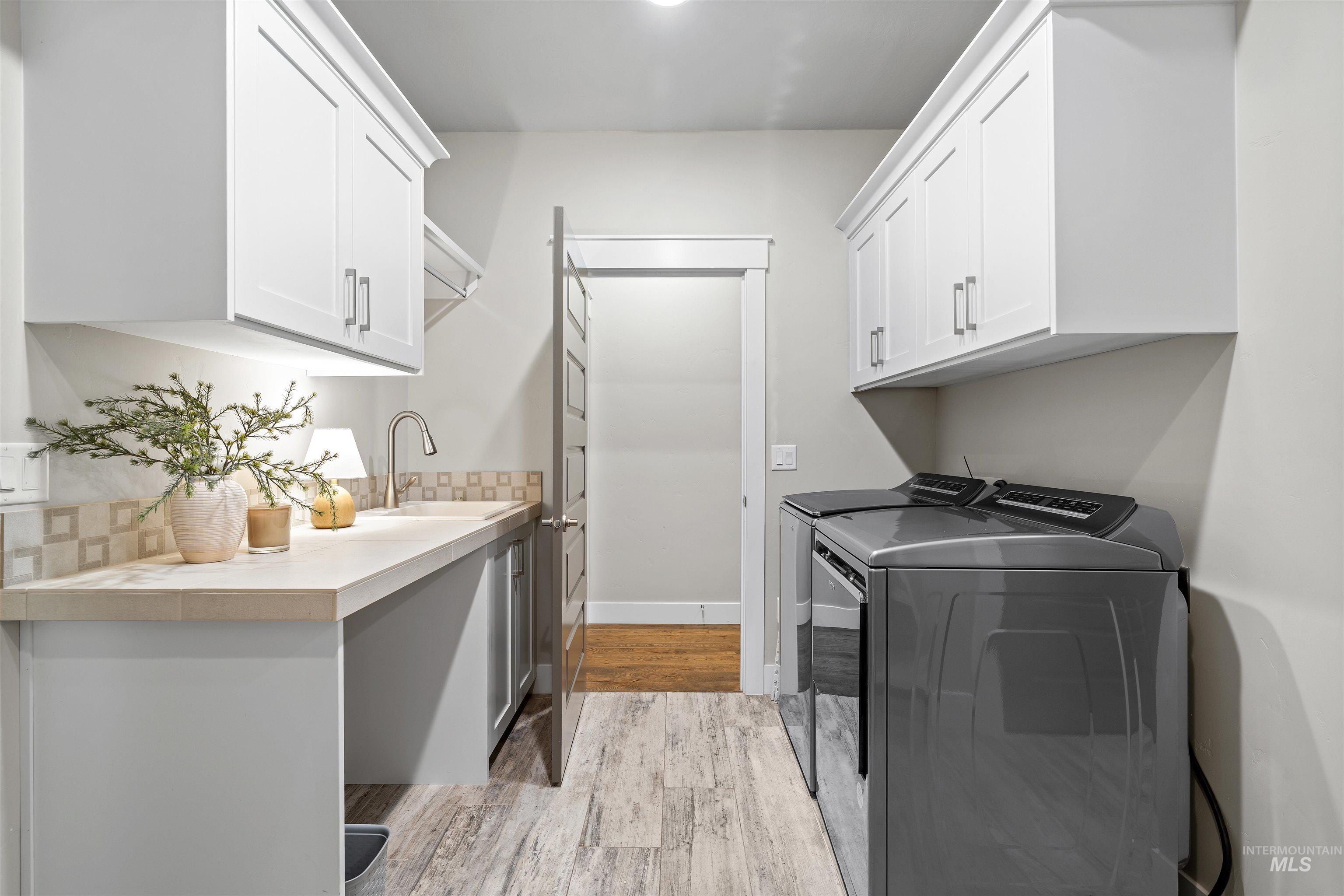 Washroom with light wood-style flooring, washing machine and dryer, and cabinet space