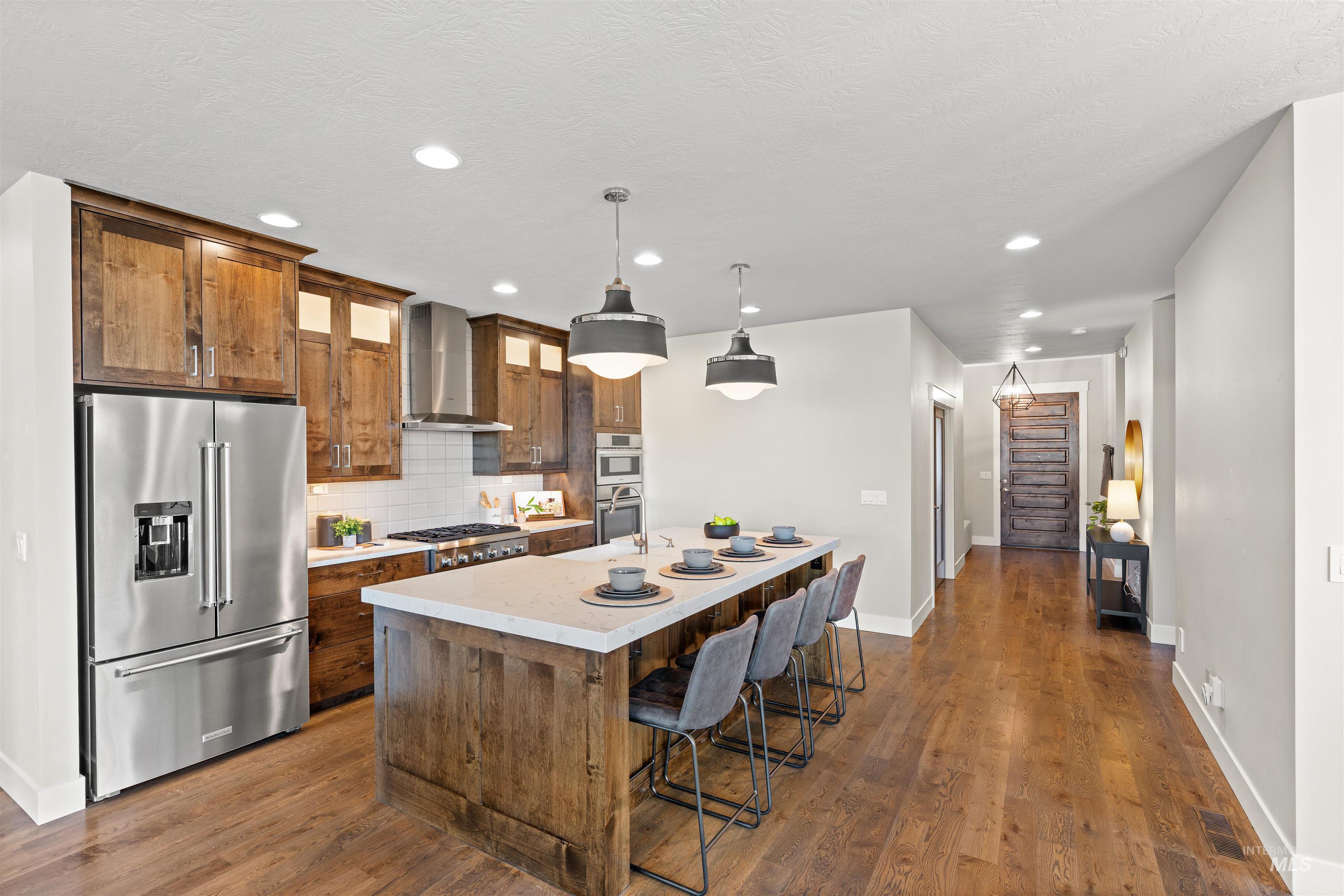 Kitchen with appliances with stainless steel finishes, hanging light fixtures, dark wood-type flooring, a breakfast bar, and a kitchen island with sink