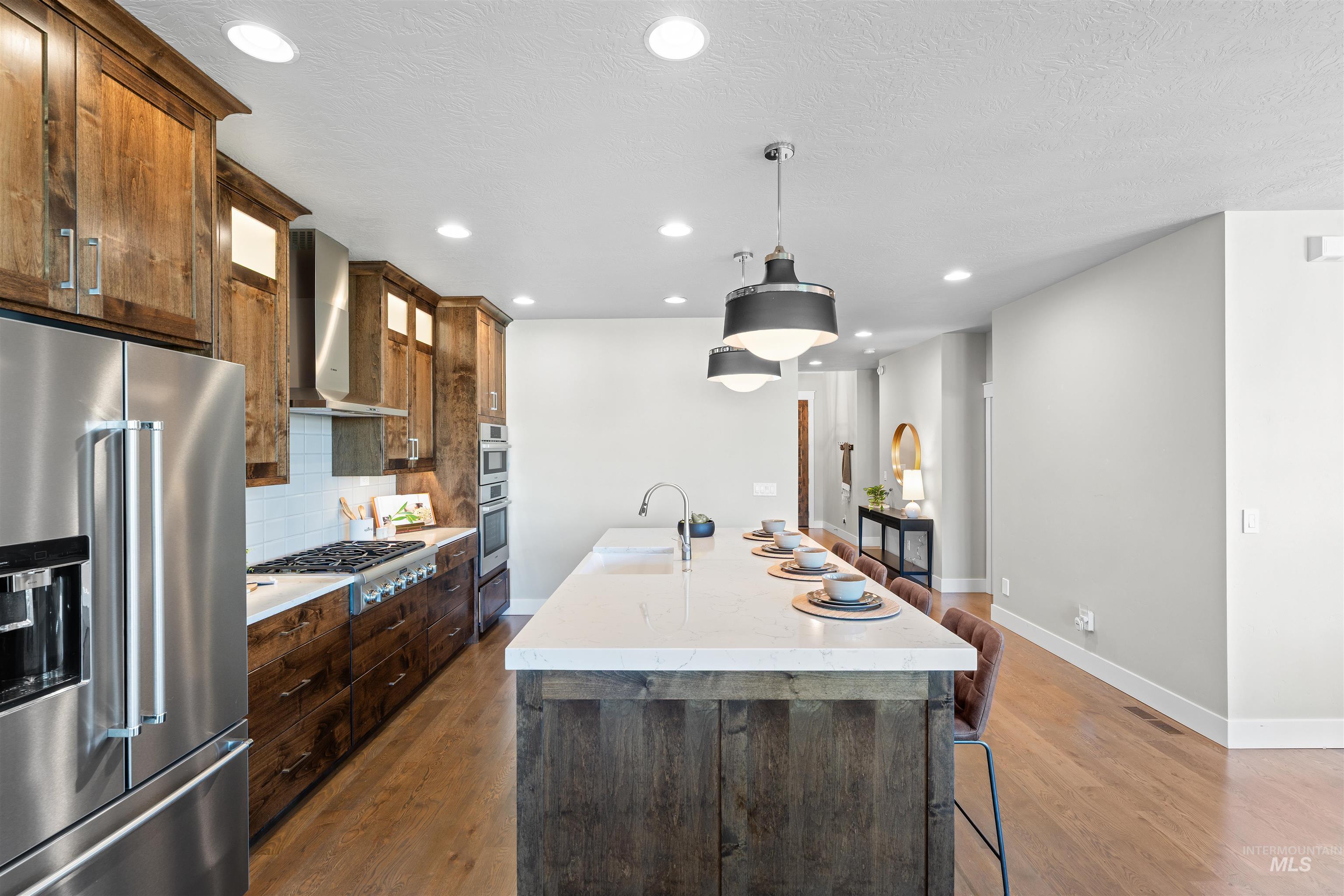 Kitchen featuring stainless steel appliances, backsplash, a center island with sink, decorative light fixtures, and recessed lighting