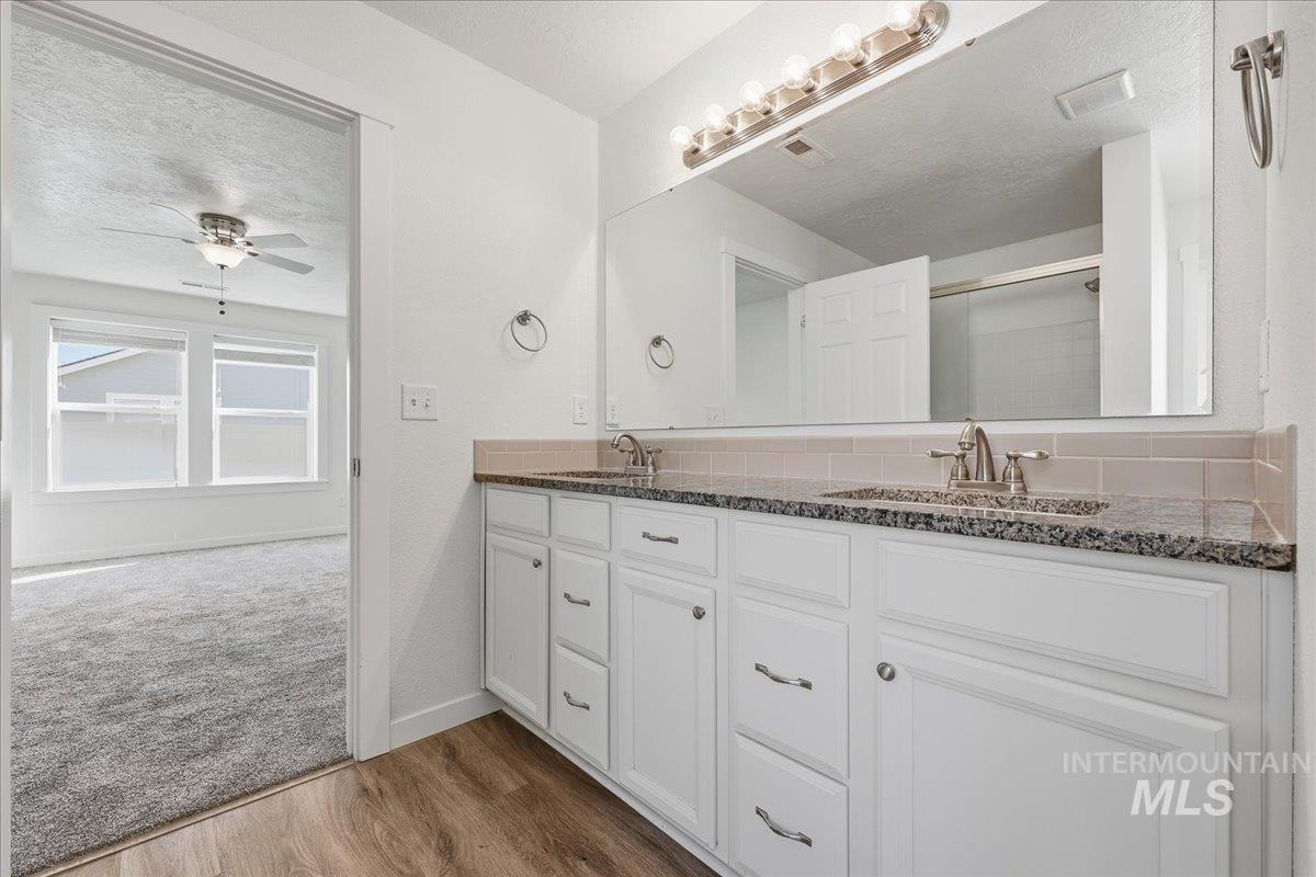 Bathroom with a textured ceiling, dark wood-style floors, double vanity, a stall shower, and a ceiling fan