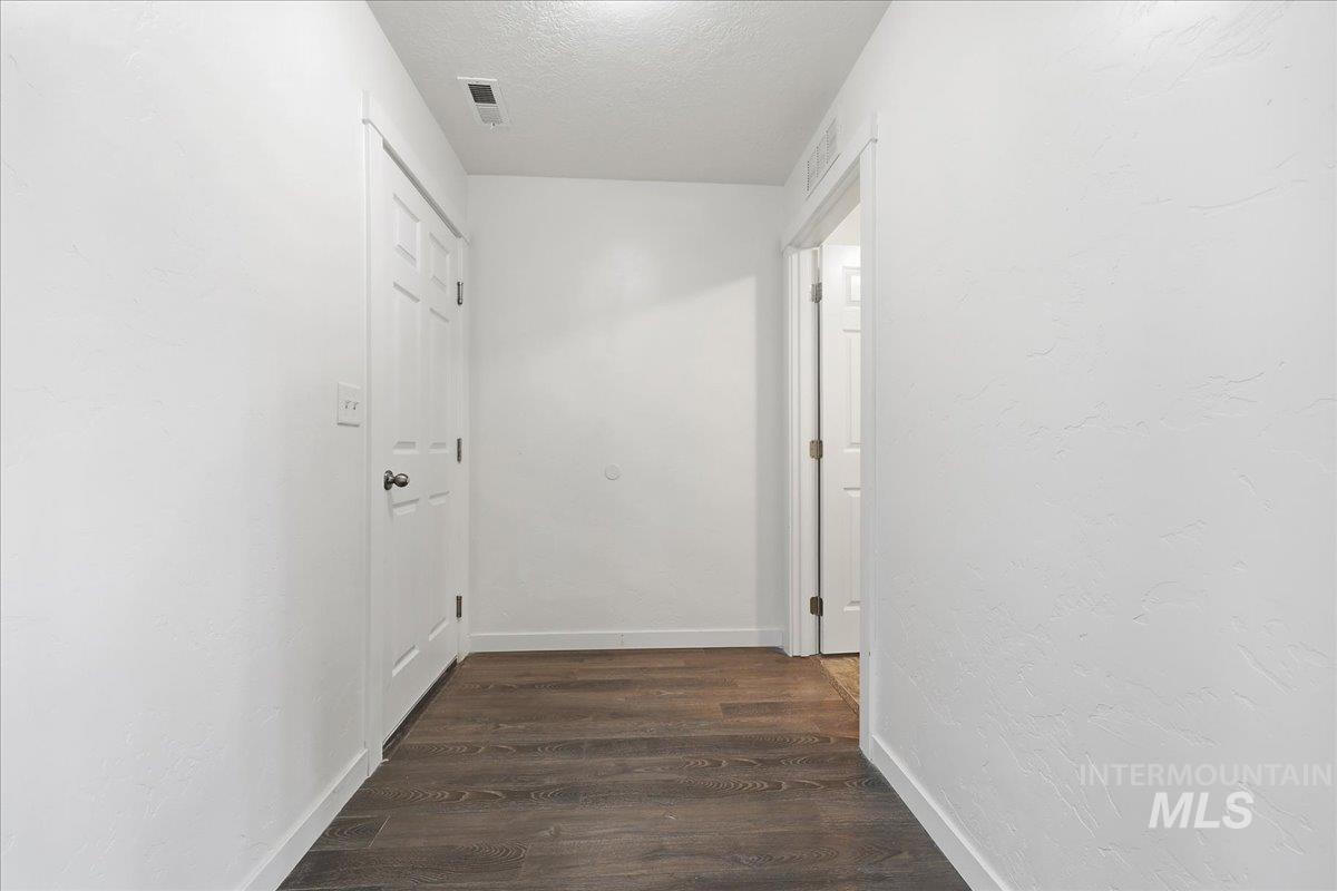 Corridor featuring dark wood-style floors, a textured ceiling, and a textured wall