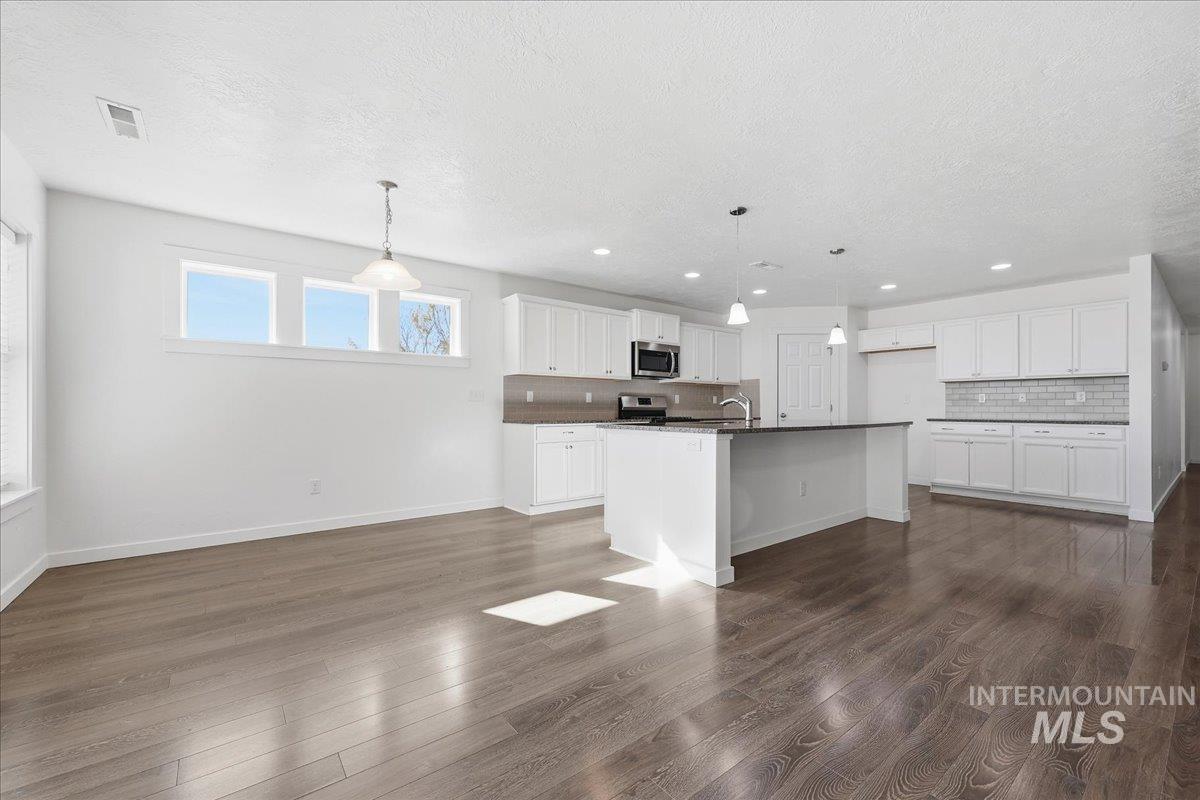 Kitchen featuring backsplash, white cabinets, a center island with sink, dark countertops, and hanging light fixtures