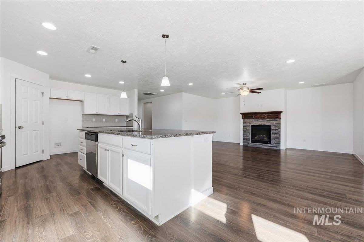 Kitchen with open floor plan, hanging light fixtures, white cabinets, dark stone counters, and dark wood-style floors