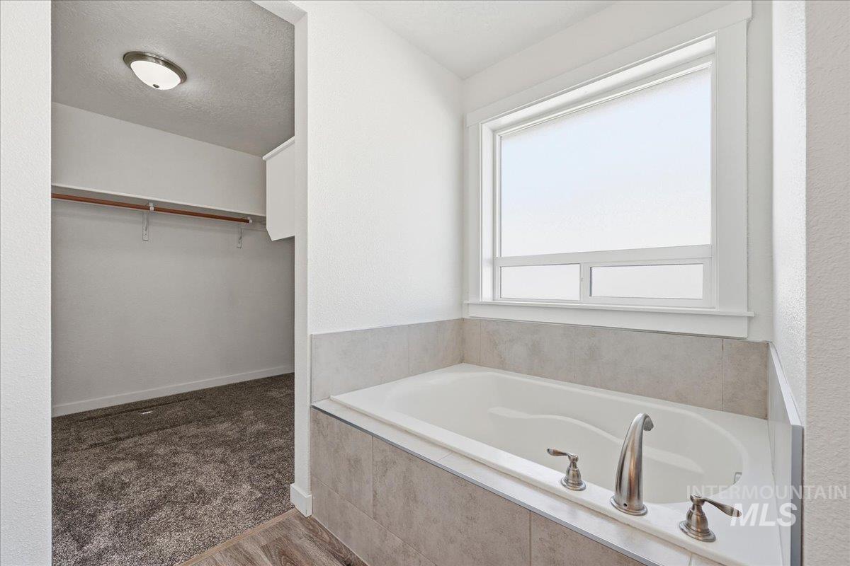 Full bath with a spacious closet, a bath, dark wood-style floors, and a textured ceiling