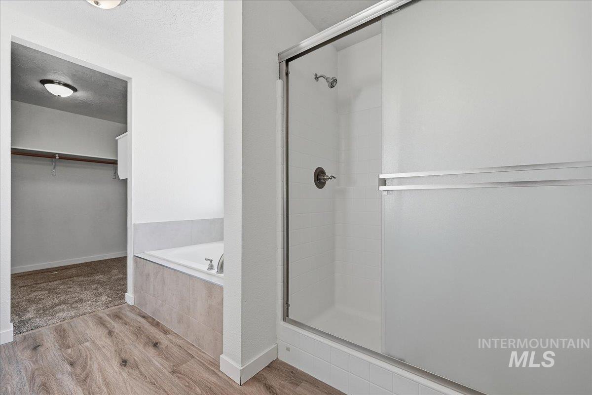 Bathroom with a spacious closet, a textured ceiling, a stall shower, wood finished floors, and a garden tub