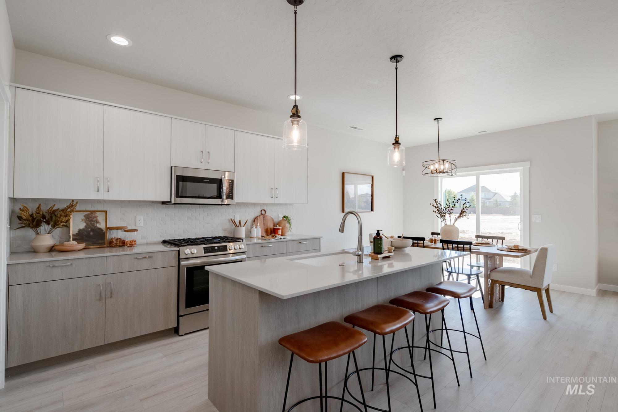 Kitchen featuring appliances with stainless steel finishes, light wood finished floors, hanging light fixtures, decorative backsplash, and a kitchen breakfast bar