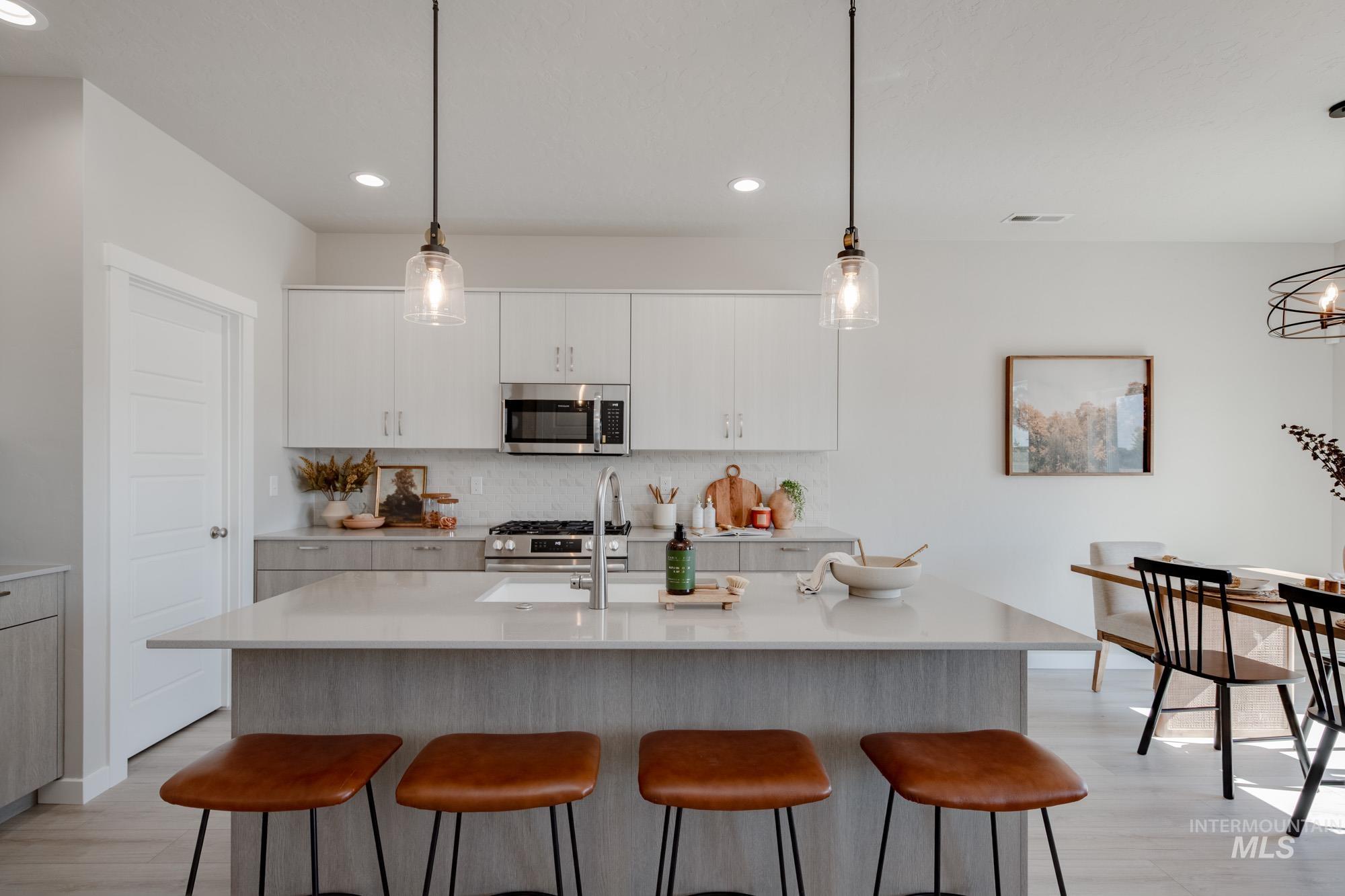 Kitchen with hanging light fixtures, backsplash, a kitchen island with sink, recessed lighting, and stainless steel appliances