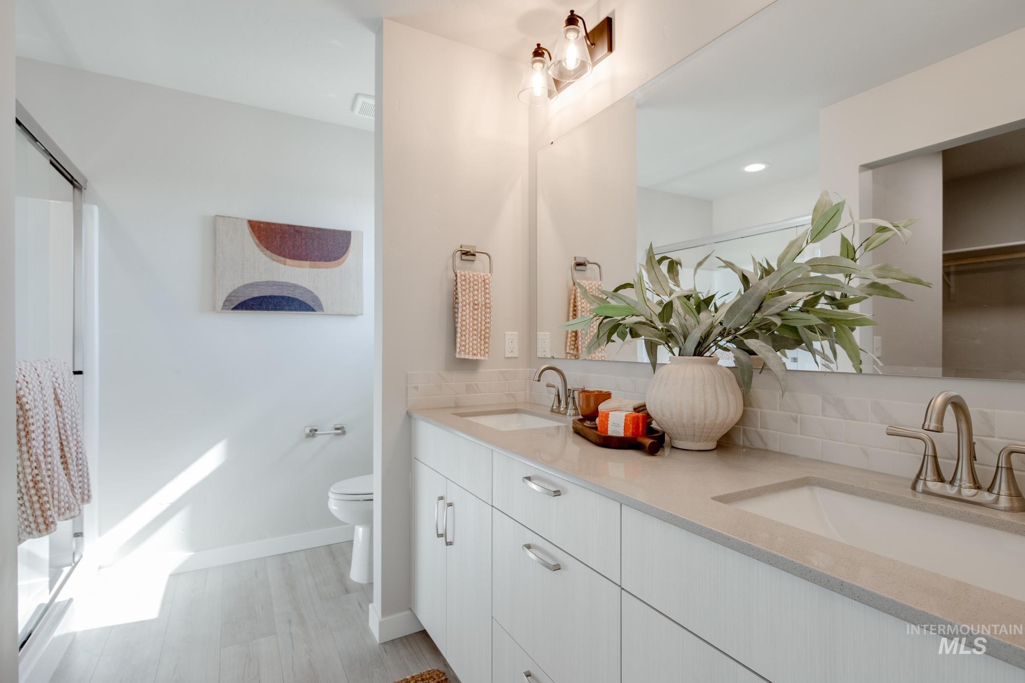 Bathroom featuring double vanity, light wood finished floors, tasteful backsplash, an enclosed shower, and recessed lighting