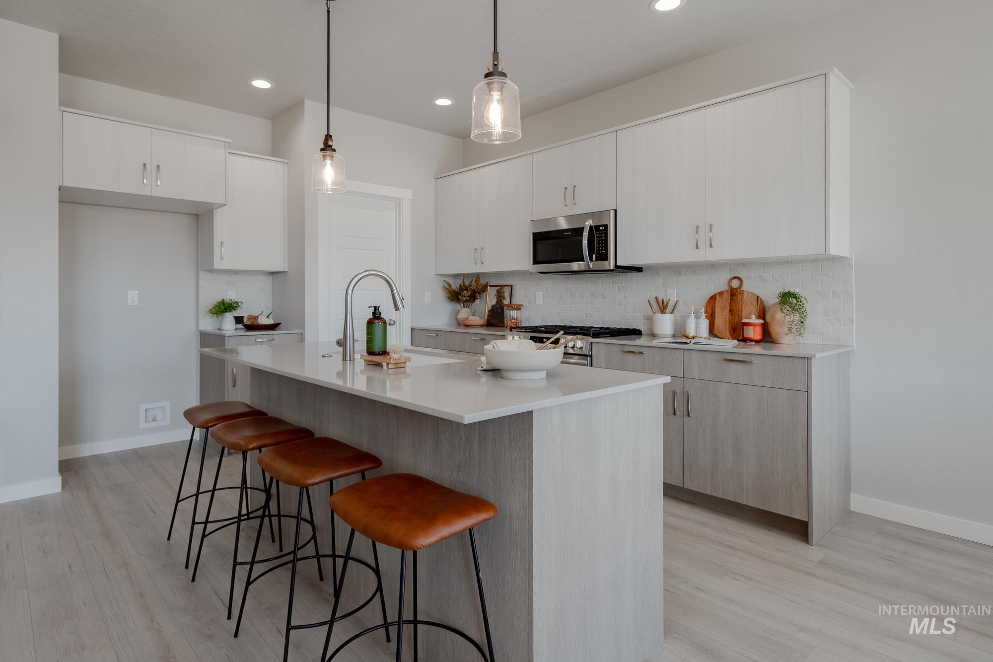Kitchen featuring an island with sink, a kitchen bar, hanging light fixtures, backsplash, and light wood-style flooring