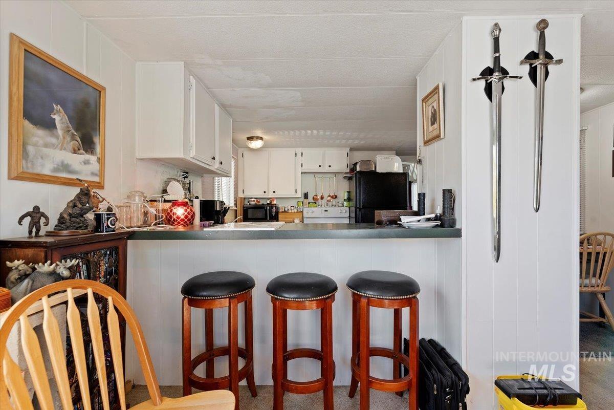 Kitchen featuring white cabinets, a breakfast bar area, black appliances, dark countertops, and a peninsula