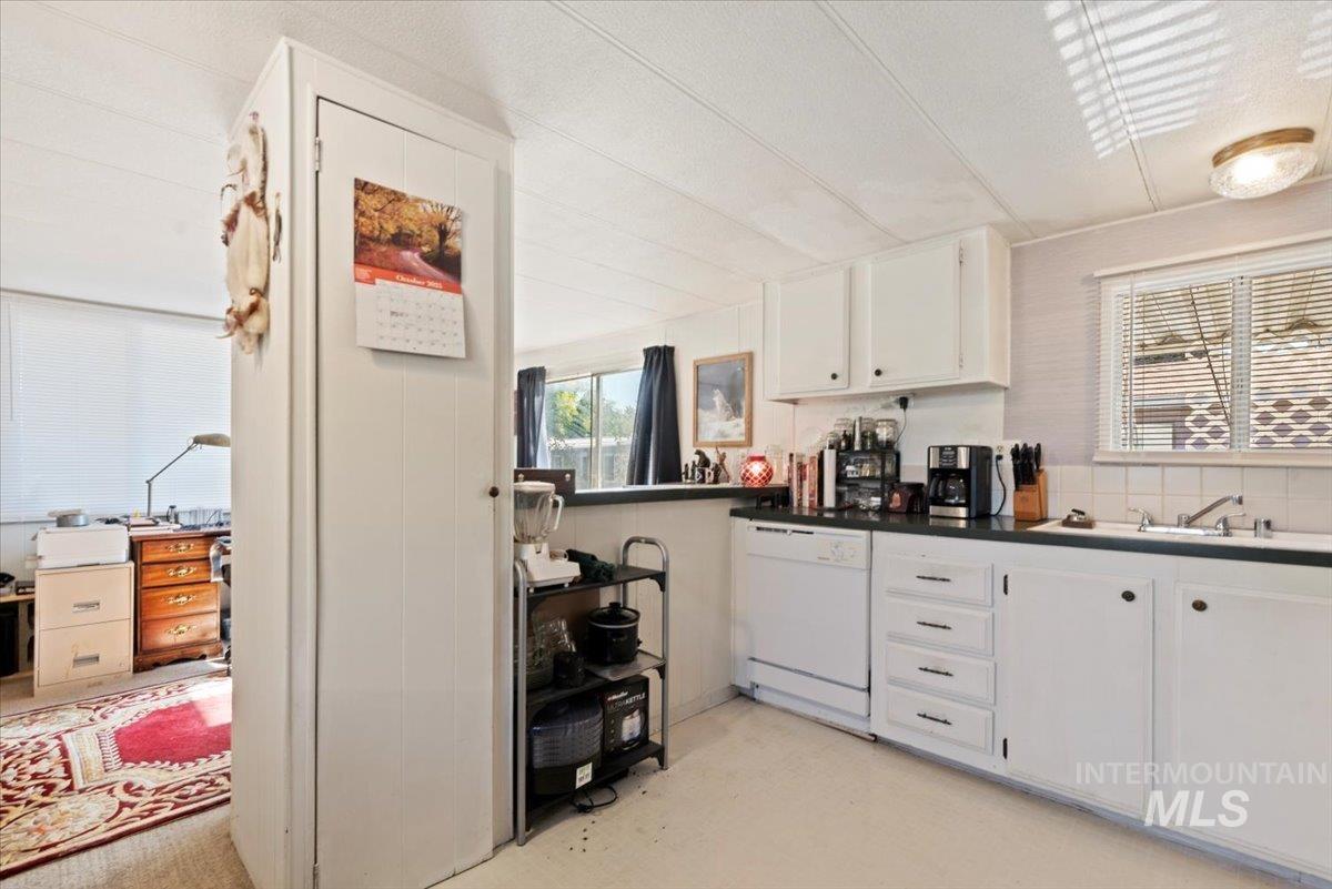 Kitchen with white cabinetry, dark countertops, white dishwasher, and concrete floors