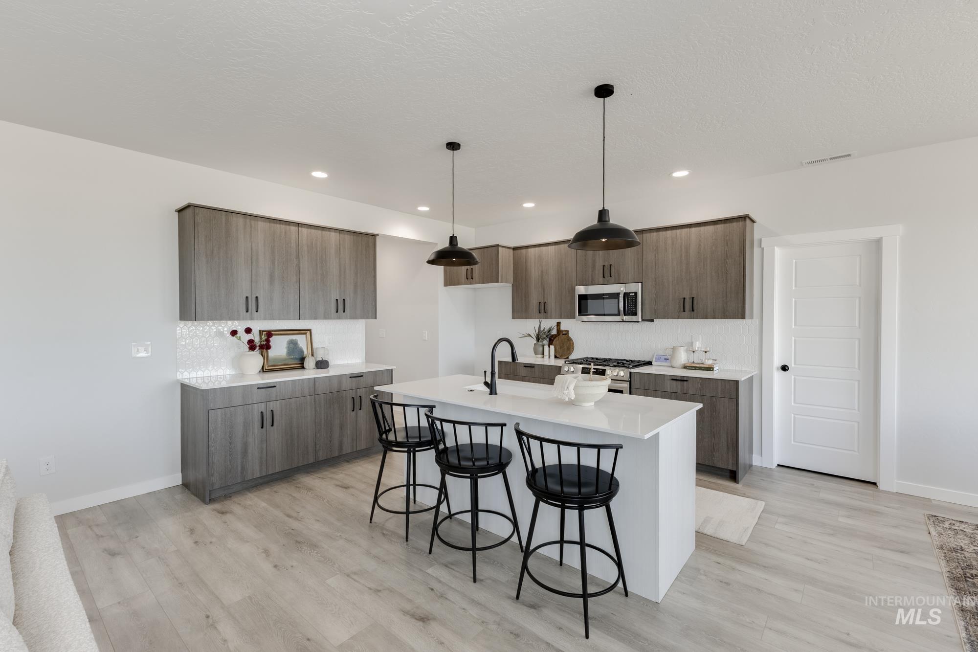 Kitchen with a kitchen bar, pendant lighting, appliances with stainless steel finishes, light stone counters, and a center island with sink
