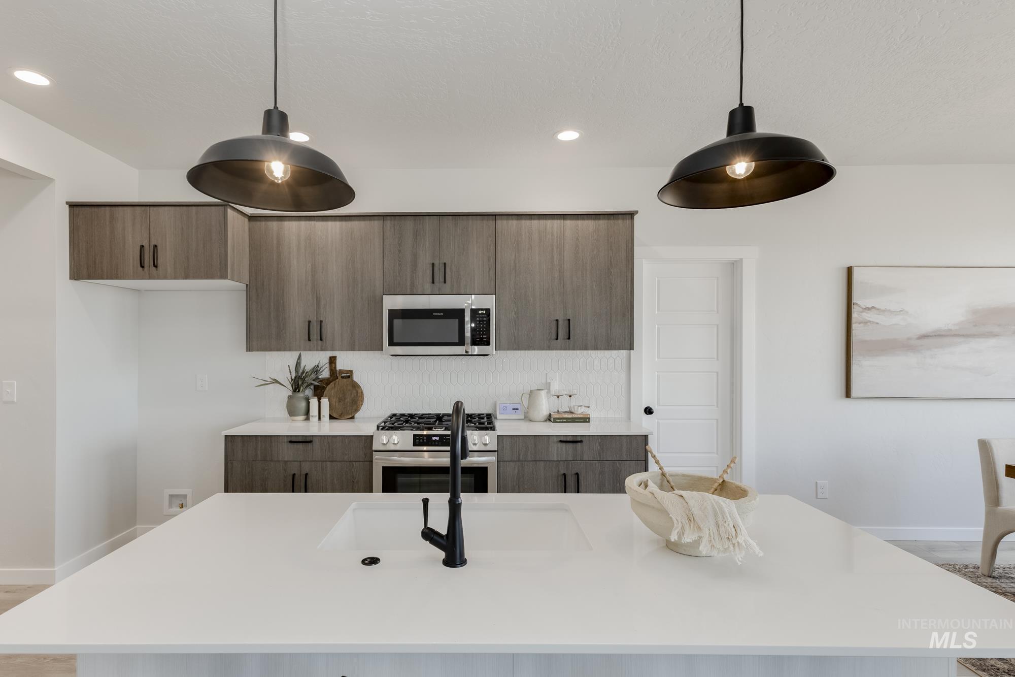 Kitchen featuring appliances with stainless steel finishes, an island with sink, modern cabinets, light stone counters, and decorative light fixtures