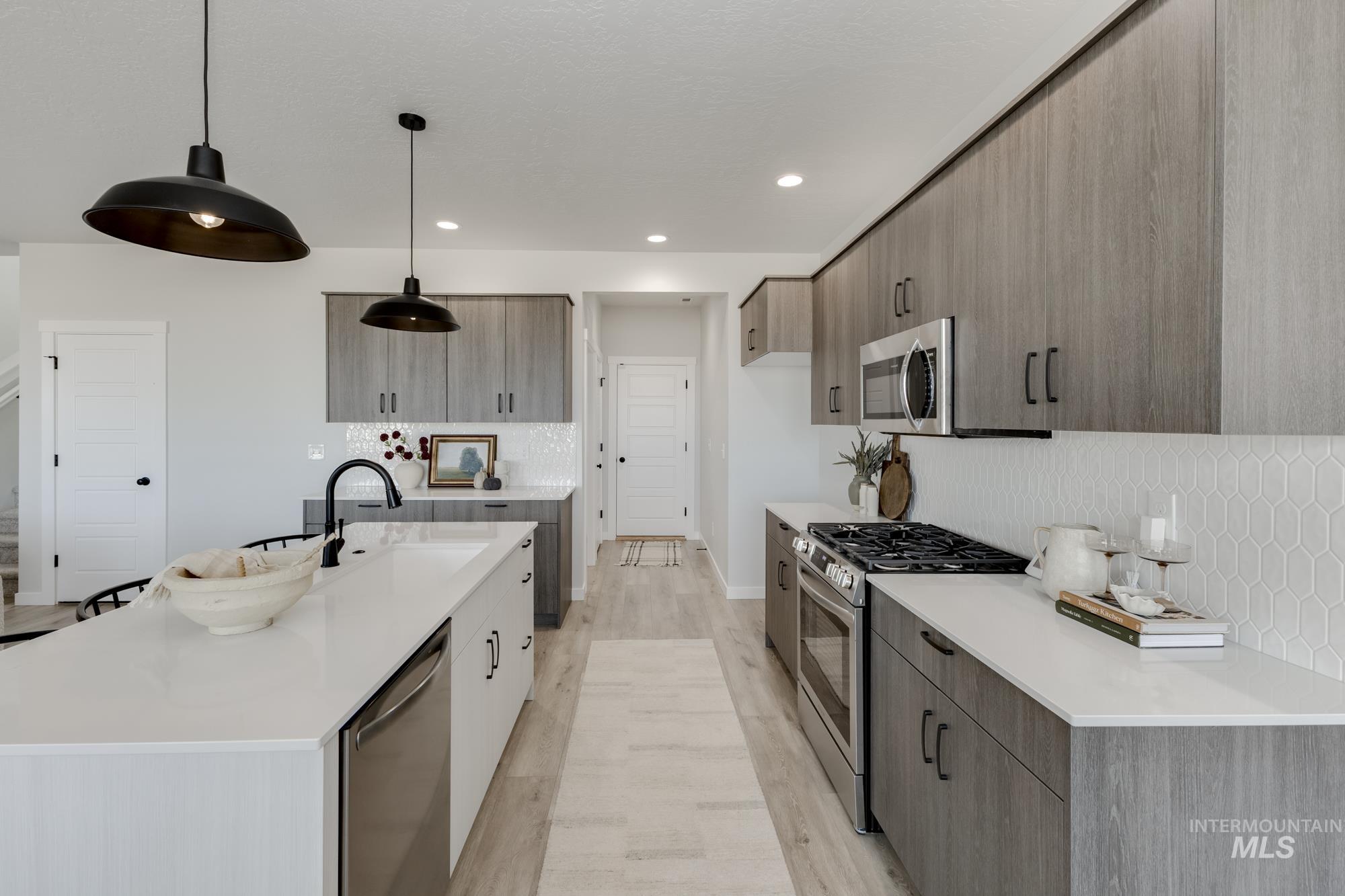 Kitchen featuring tasteful backsplash, appliances with stainless steel finishes, modern cabinets, light wood-type flooring, and hanging light fixtures