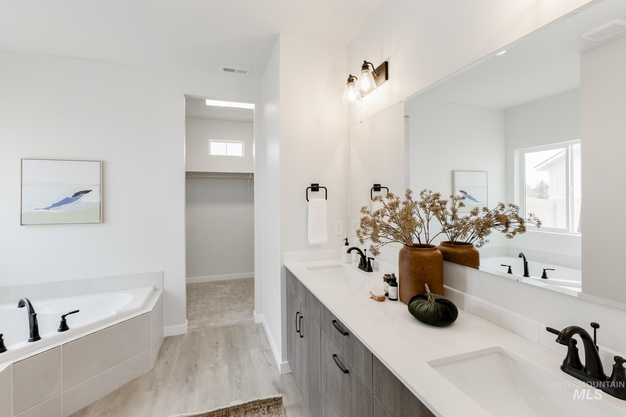 Bathroom featuring a garden tub, double vanity, a spacious closet, and light wood-type flooring