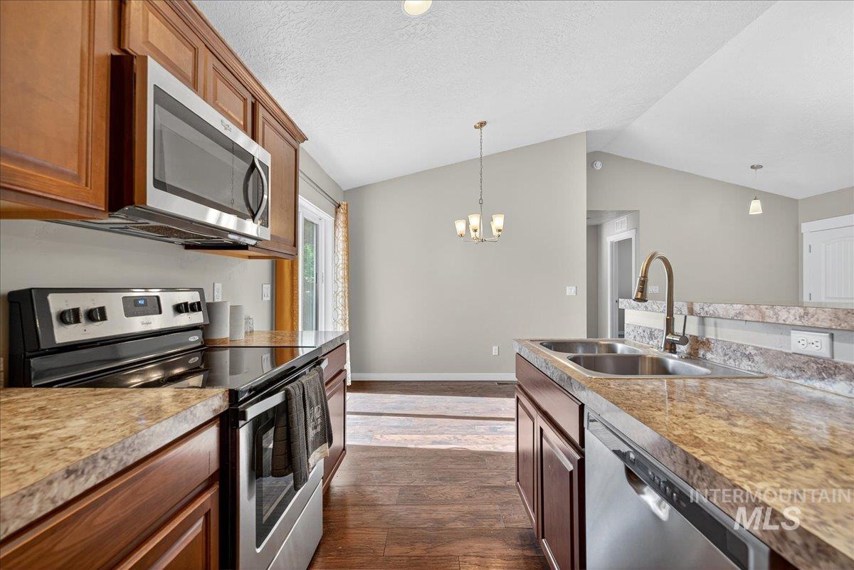 Kitchen with stainless steel appliances, dark wood-type flooring, vaulted ceiling, light countertops, and hanging light fixtures