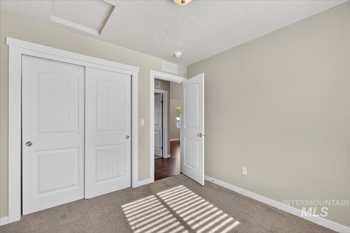 Unfurnished bedroom with carpet, a textured ceiling, a closet, and attic access