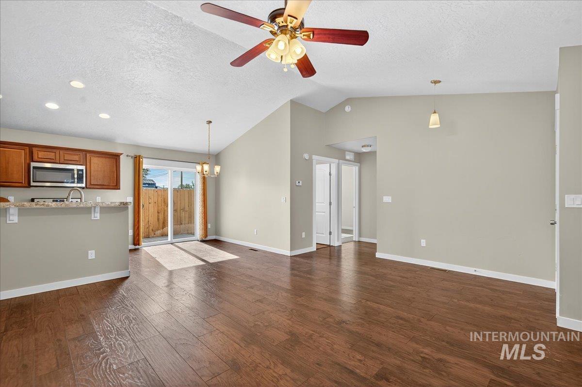 Unfurnished living room with dark wood-style flooring, a chandelier, vaulted ceiling, a textured ceiling, and a ceiling fan