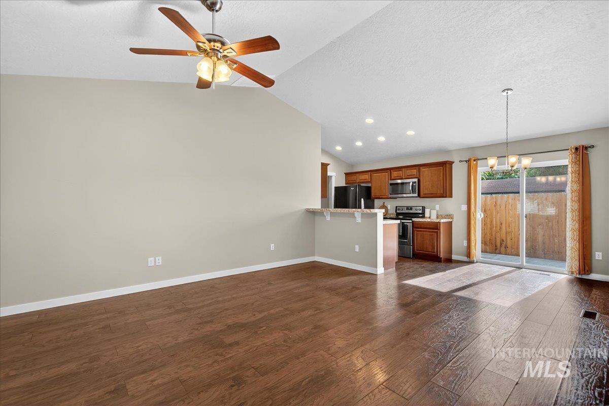 Unfurnished living room featuring vaulted ceiling, dark wood finished floors, a ceiling fan, a chandelier, and a textured ceiling