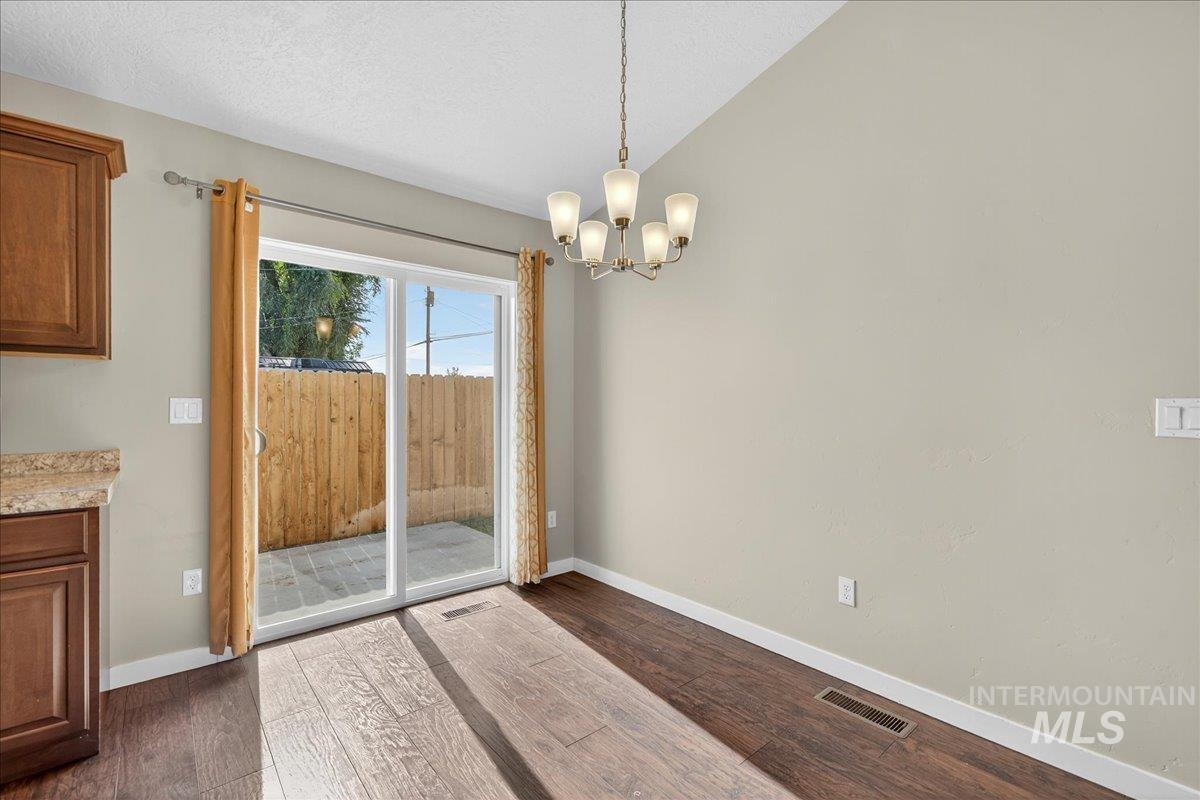 Unfurnished dining area featuring dark wood-type flooring, a chandelier, vaulted ceiling, and a textured ceiling
