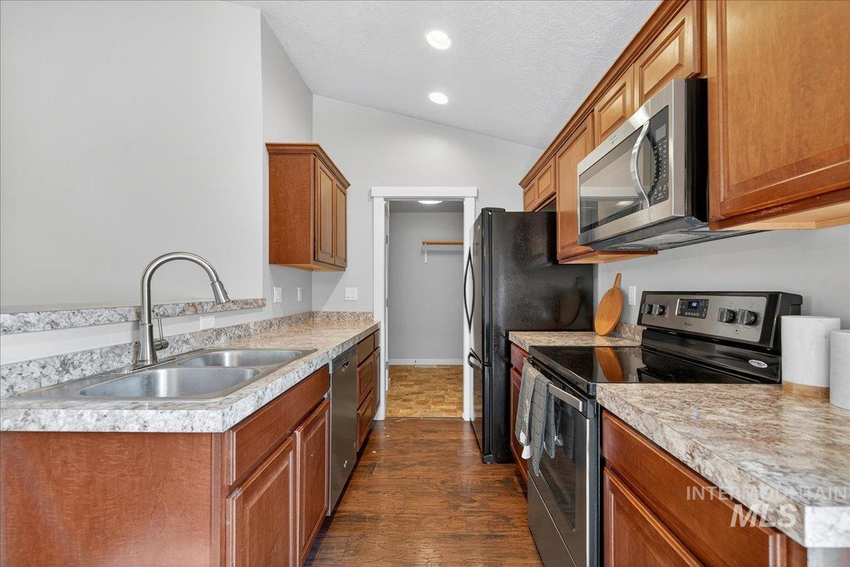 Kitchen featuring appliances with stainless steel finishes, brown cabinetry, dark wood-style flooring, vaulted ceiling, and light countertops