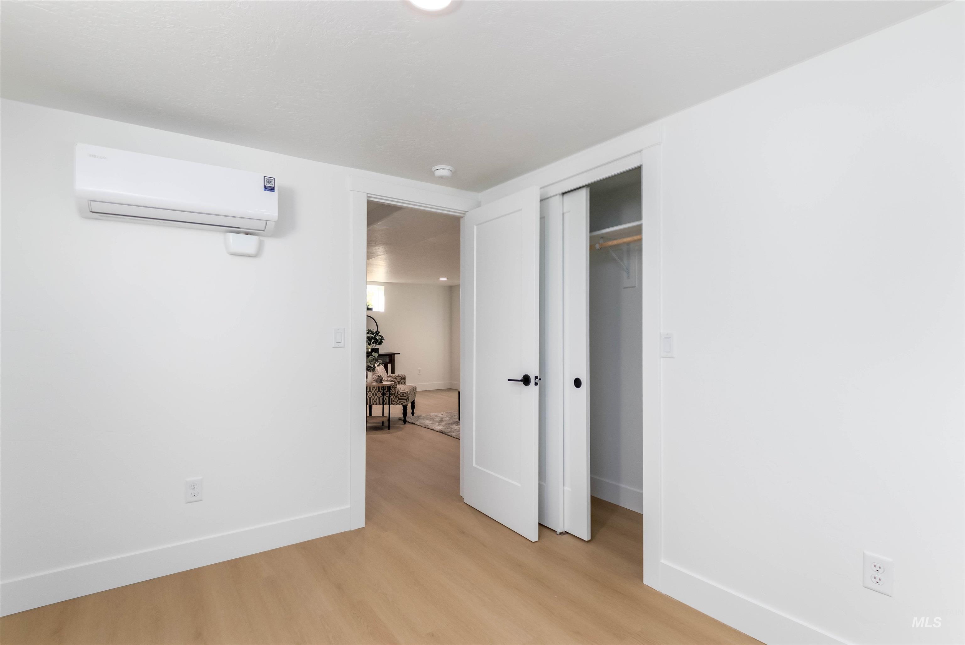Unfurnished bedroom featuring light wood-type flooring, a closet, and a wall unit AC