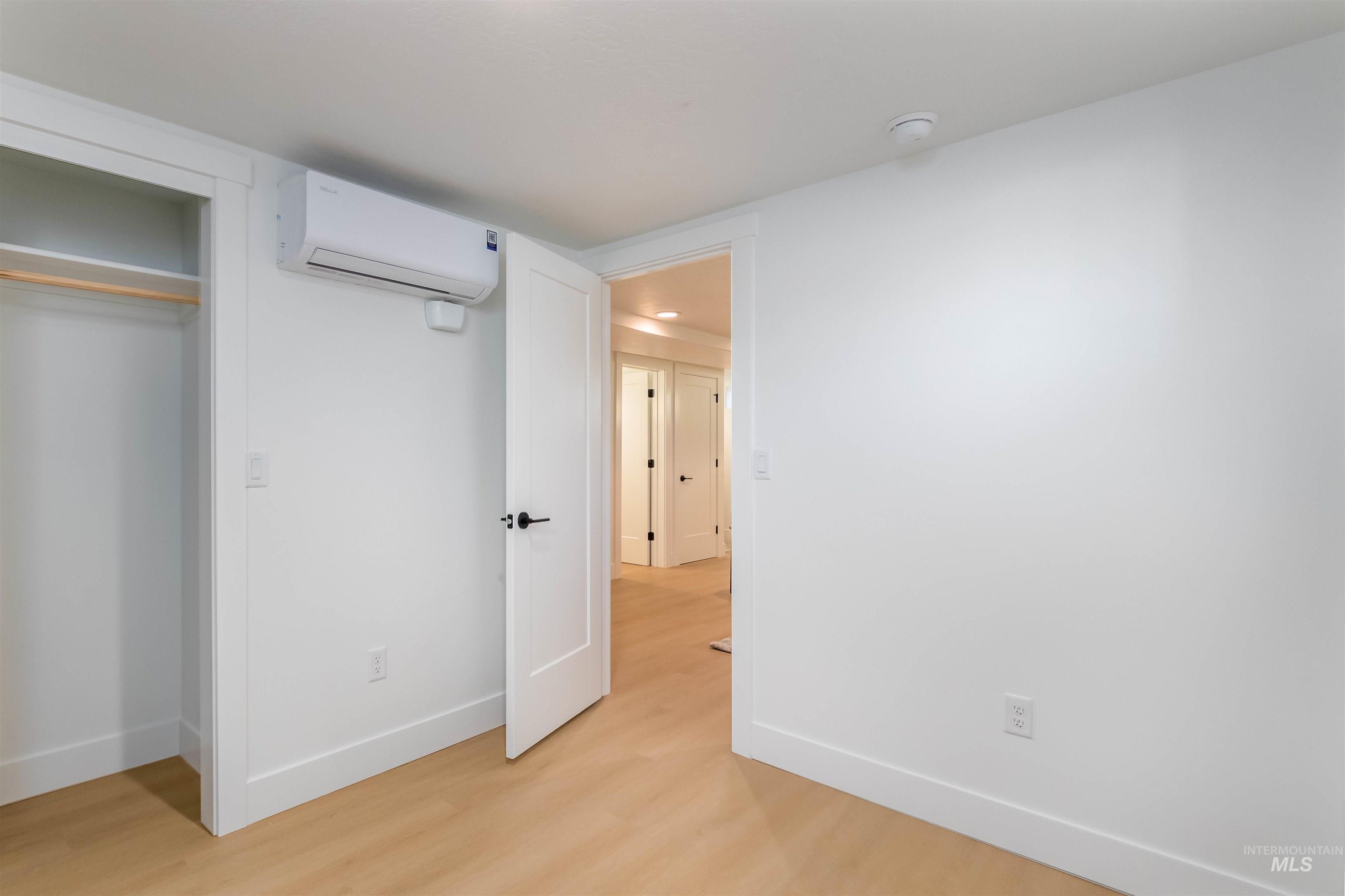 Unfurnished bedroom with light wood-style floors, a wall unit AC, and a closet