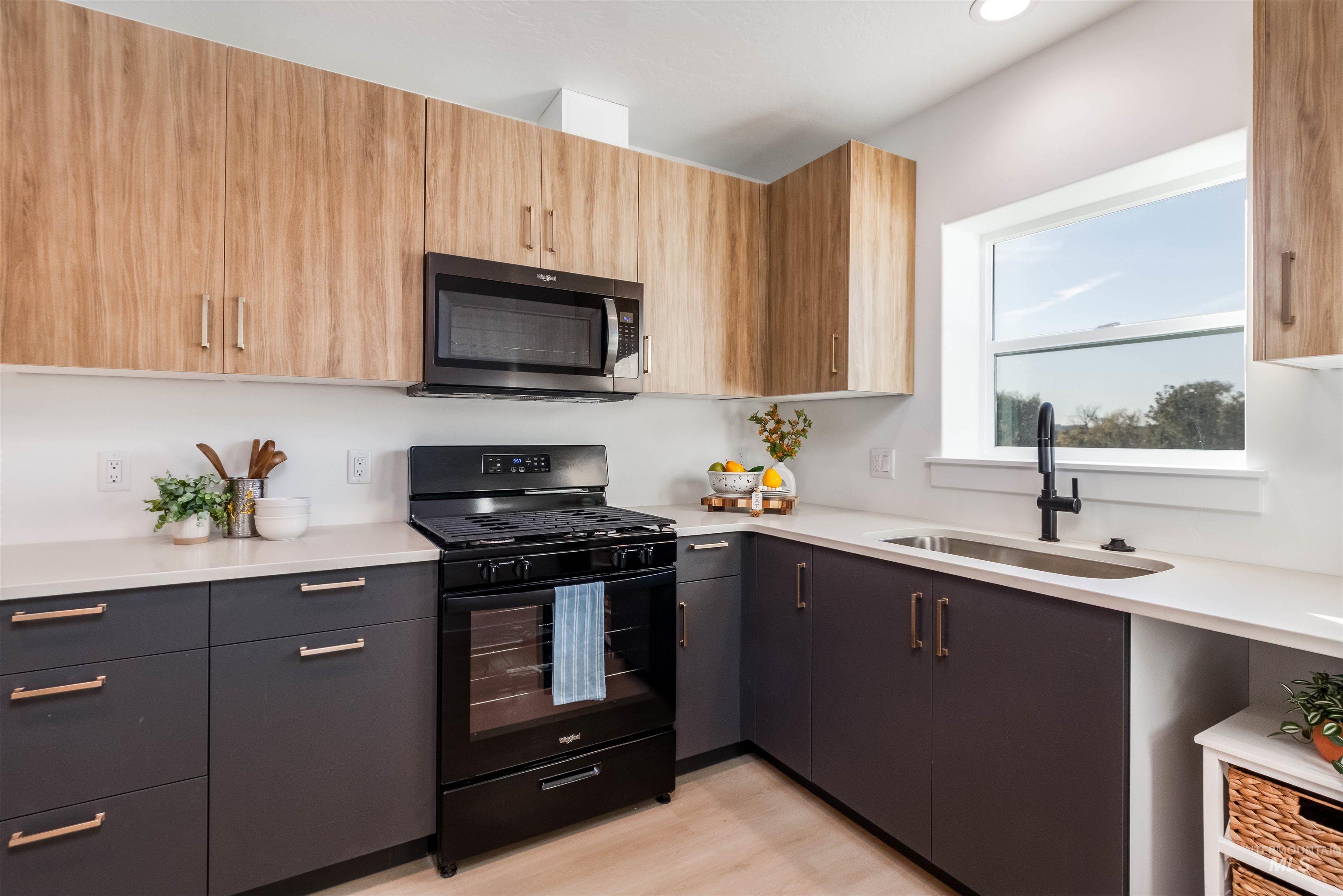 Kitchen featuring black gas range oven, modern cabinets, stainless steel microwave, light wood finished floors, and light stone counters