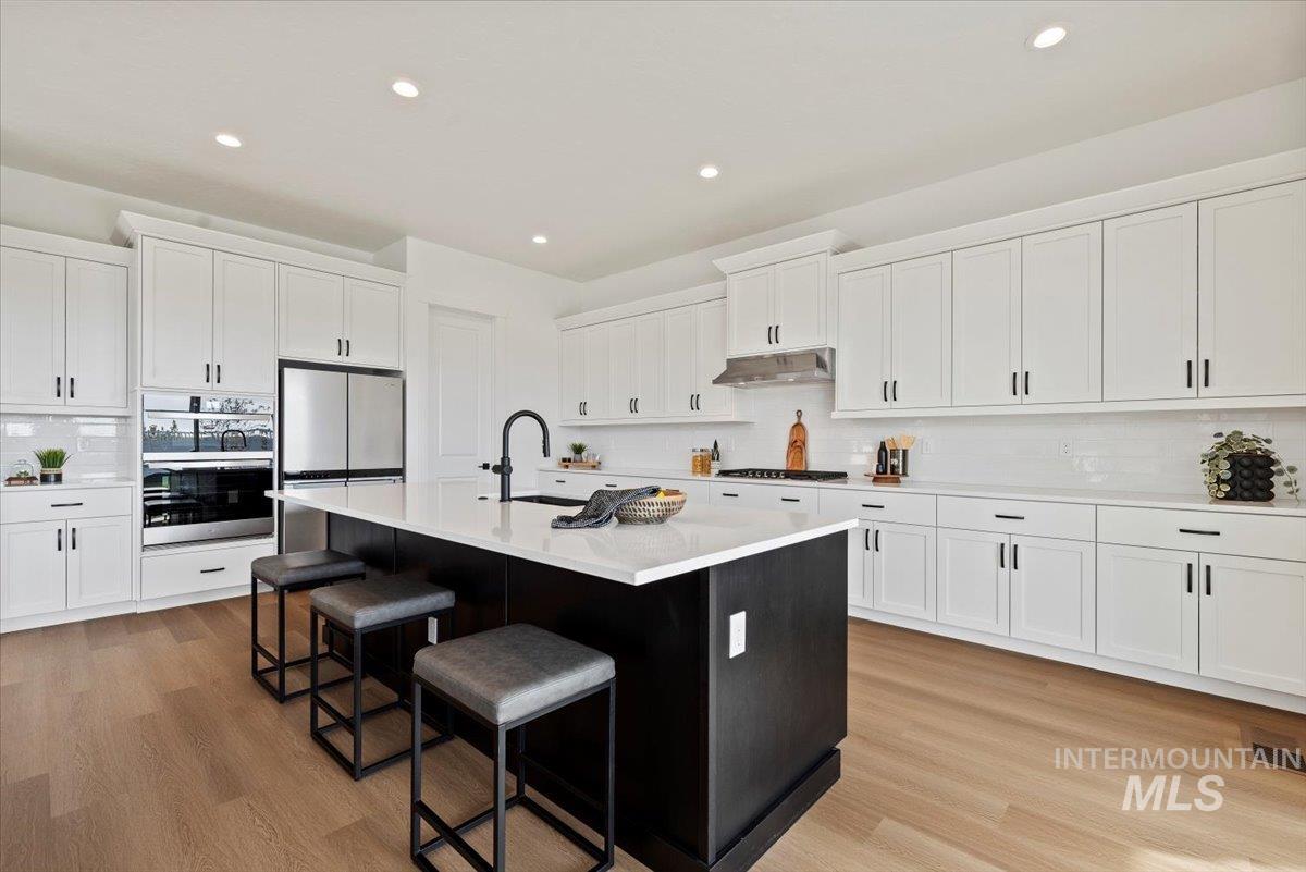 Kitchen featuring decorative backsplash, white cabinets, appliances with stainless steel finishes, a center island with sink, and recessed lighting