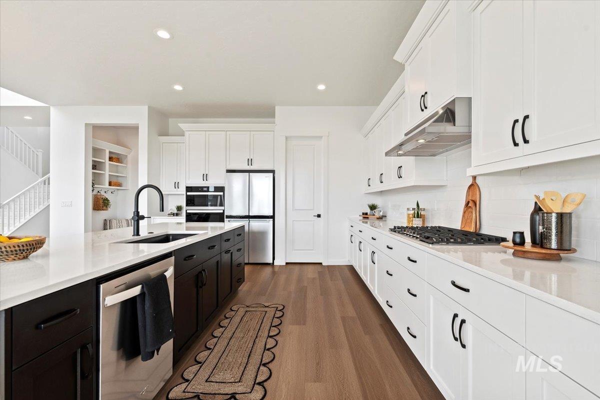Kitchen with white cabinetry, stainless steel appliances, dark wood-type flooring, light stone counters, and recessed lighting