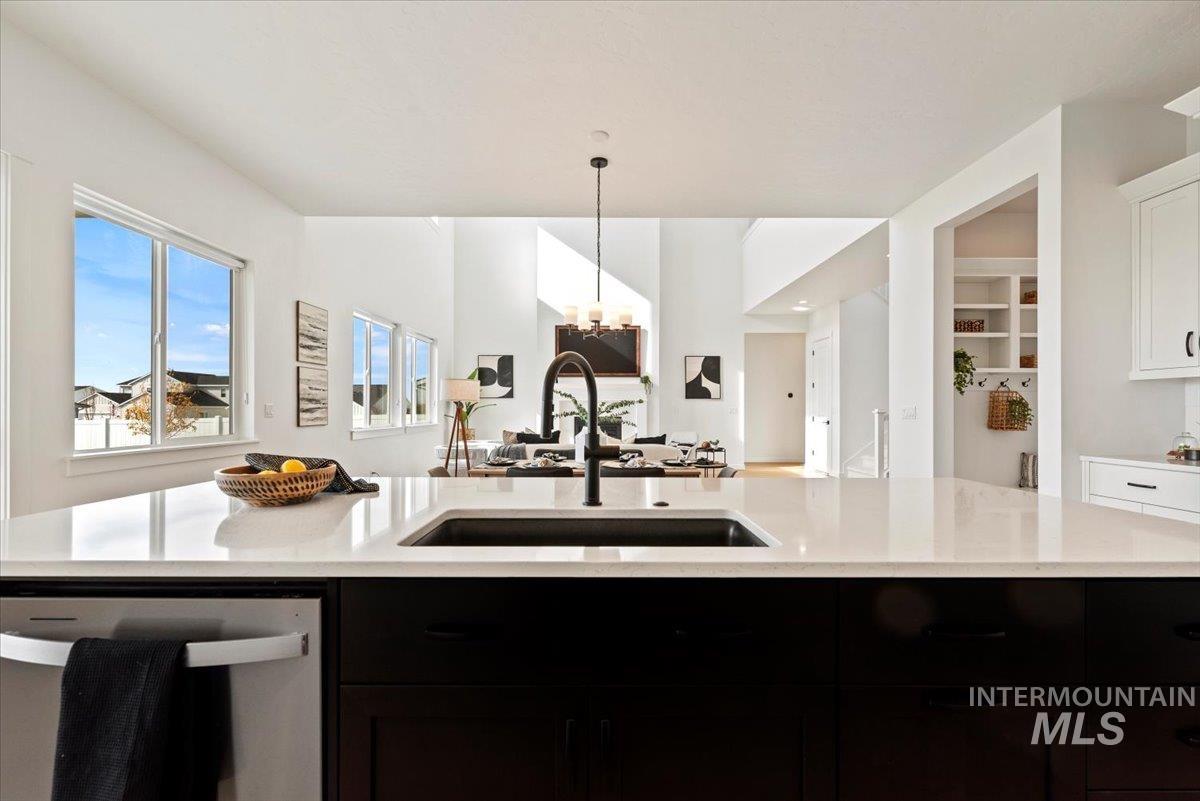 Kitchen with stainless steel dishwasher, dark cabinetry, open floor plan, and pendant lighting