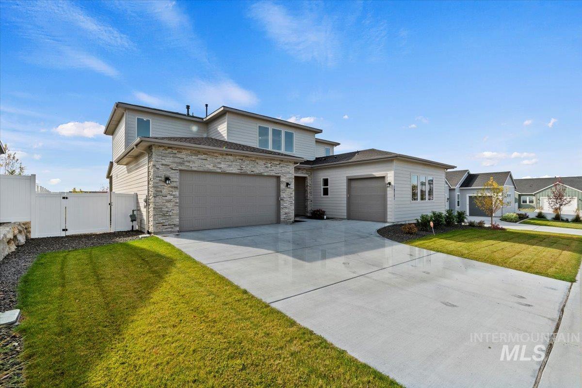 View of front of home with a gate, driveway, a garage, and stone siding
